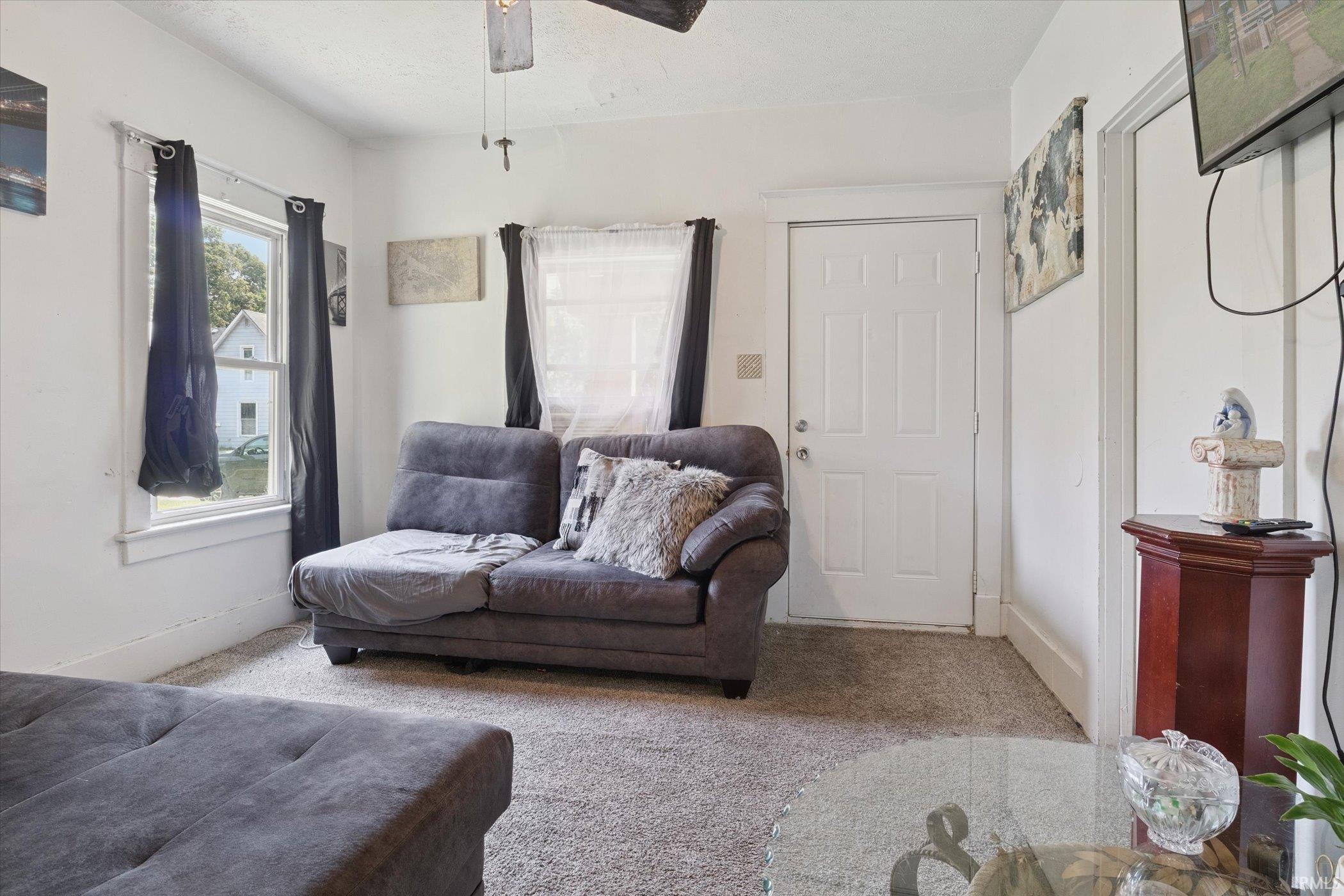 Living area with neutral carpeting, white walls, and a prominent white entry door