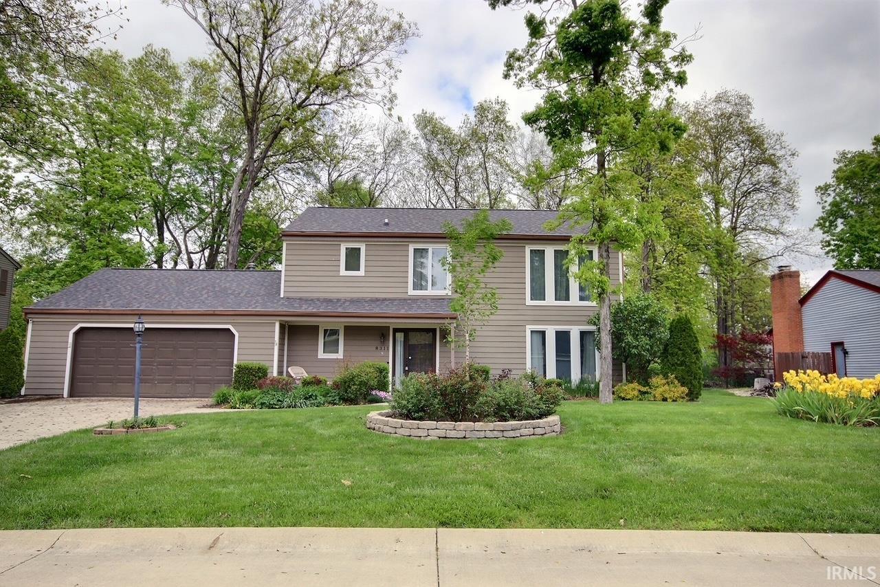 Two-story property featuring tan siding, an attached two-car garage with a brown door, and a dark shingle roof