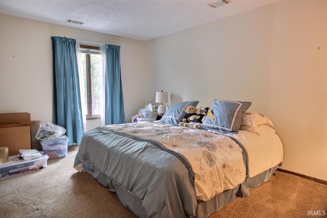Carpeted room featuring a window with a wood-finish frame, light-colored walls, and a textured ceiling