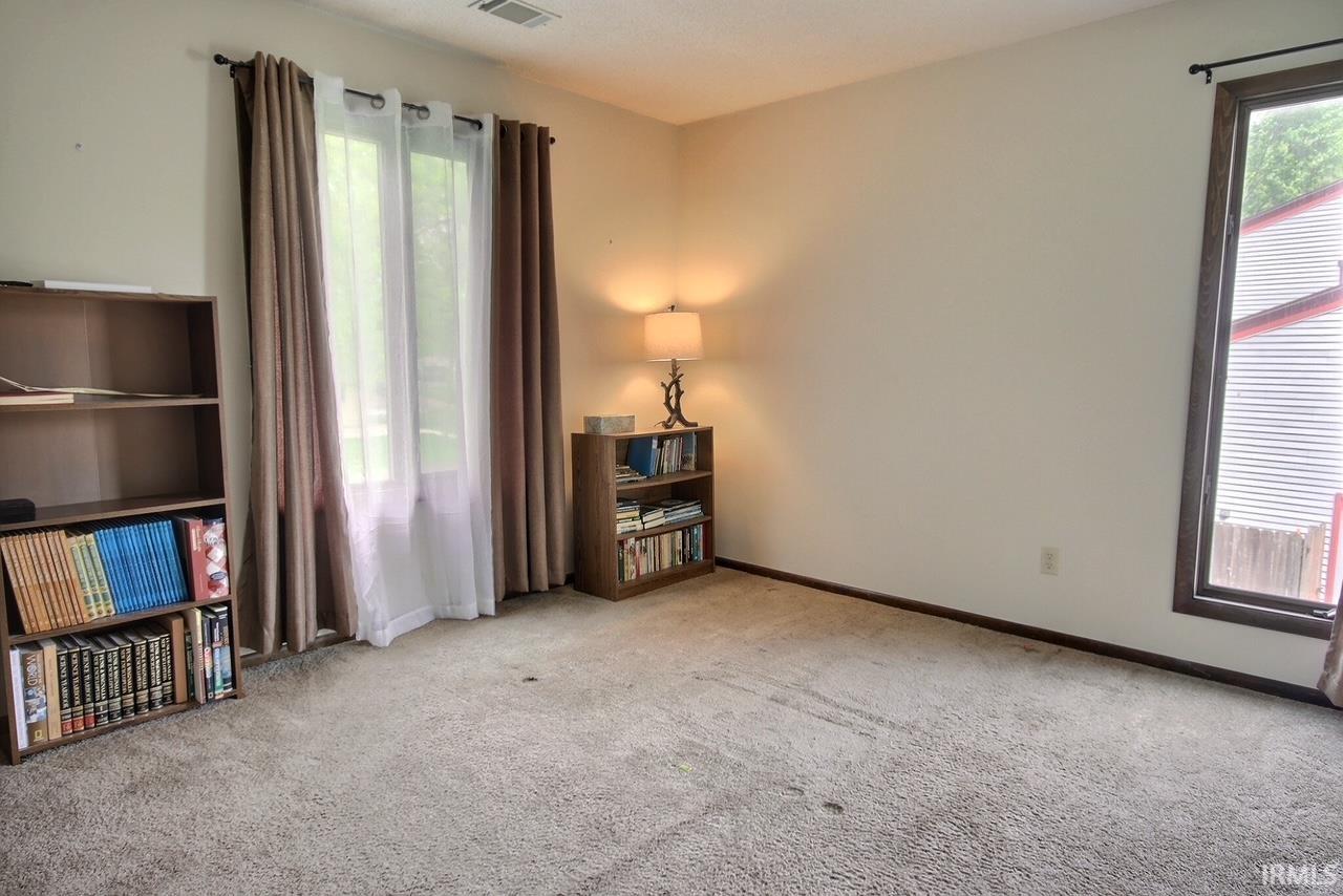 Carpeted room with a large window featuring sheer and opaque drapes