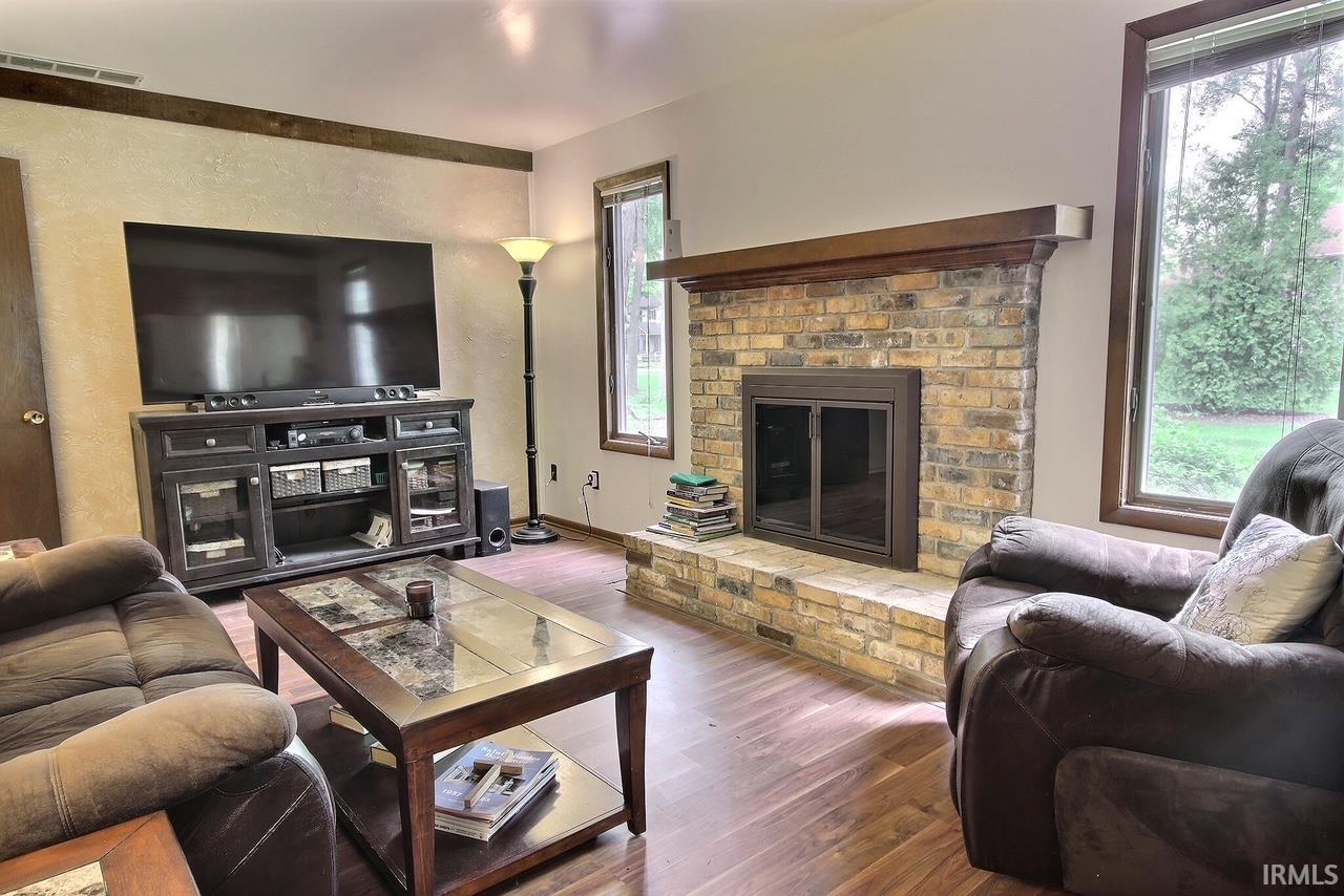 Family room featuring a brick fireplace with a wood mantel, wood-finish flooring, and large windows
