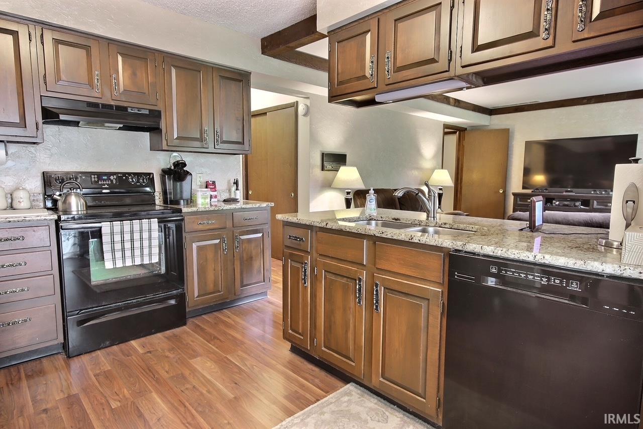 Kitchen featuring wood-finish flooring, wood cabinetry with dark hardware, granite countertops, and a black appliance suite including a range and dishwasher