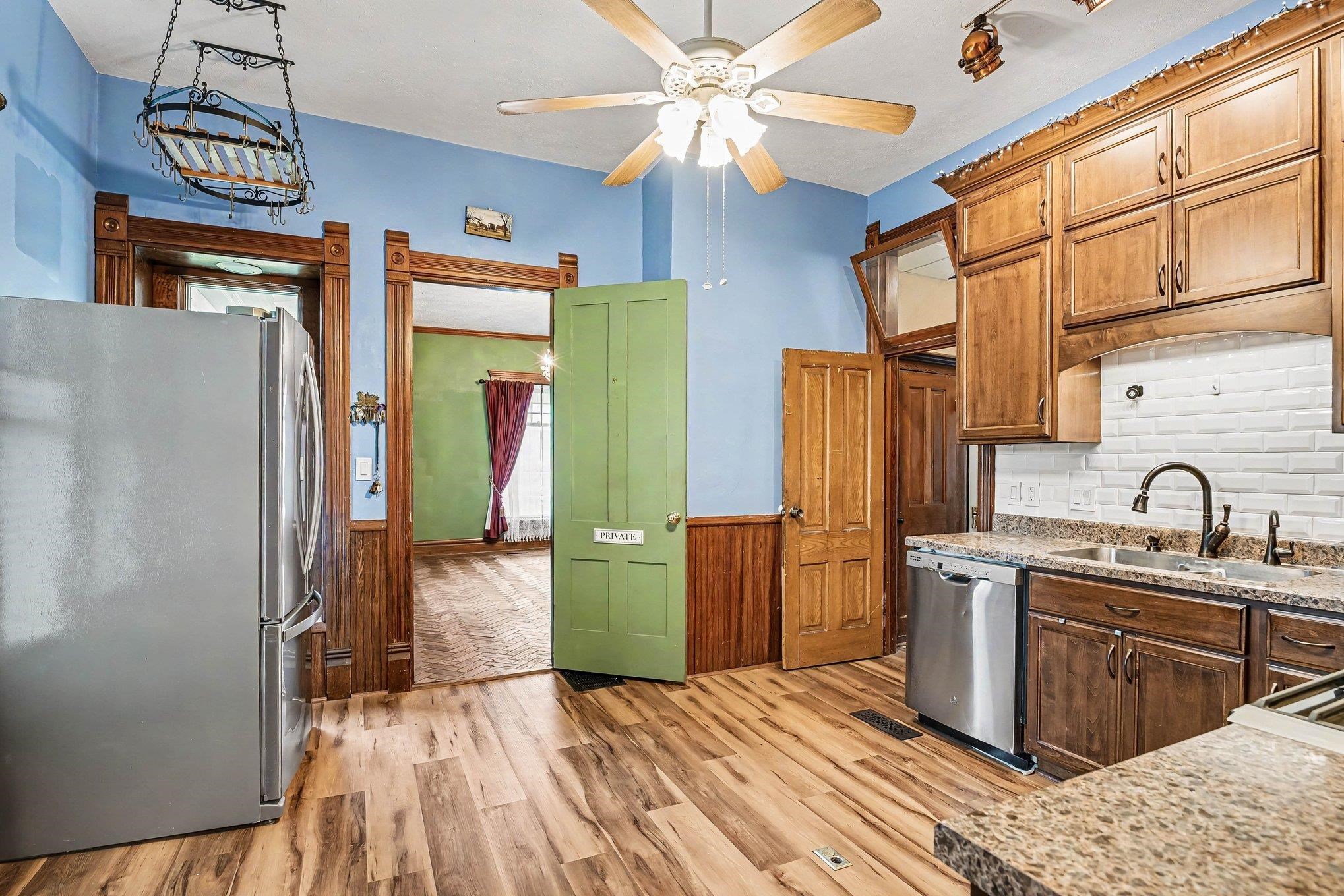 Kitchen featuring wood-finish flooring, wood cabinetry with dark hardware, a stainless steel dishwasher, a granite-patterned countertop, and a white subway tile backsplash