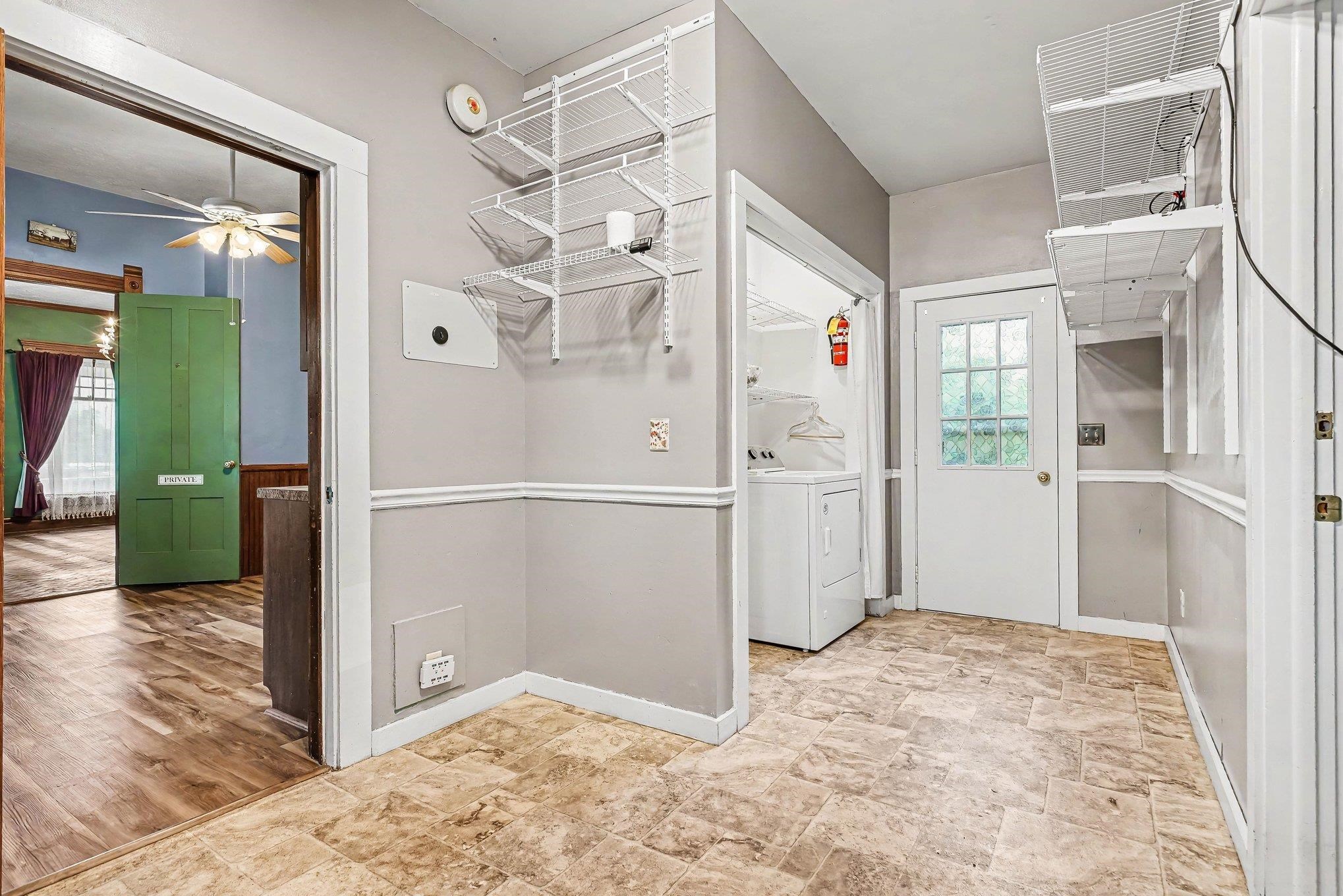Utility area featuring durable tile-look flooring, white paneled door with windowpanes, and white wall shelving