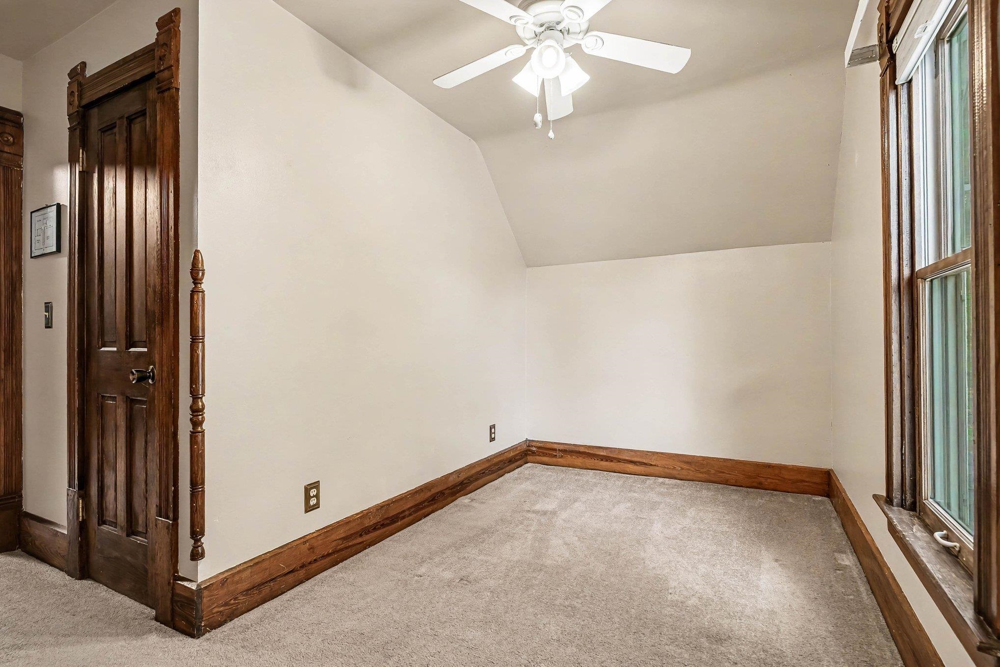 Carpeted room featuring a ceiling fan, a window with wood trim, and a paneled wood door with ornate trim