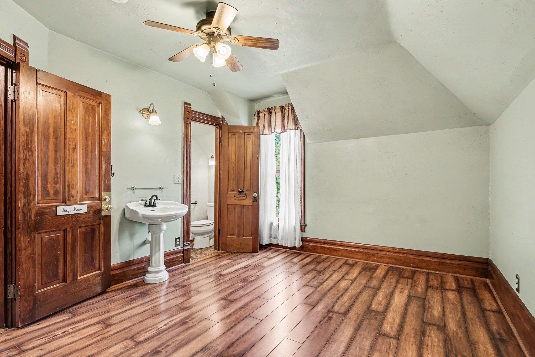 Room featuring wood-finish flooring, a ceiling fan with integrated lighting, and a window with white sheer curtains