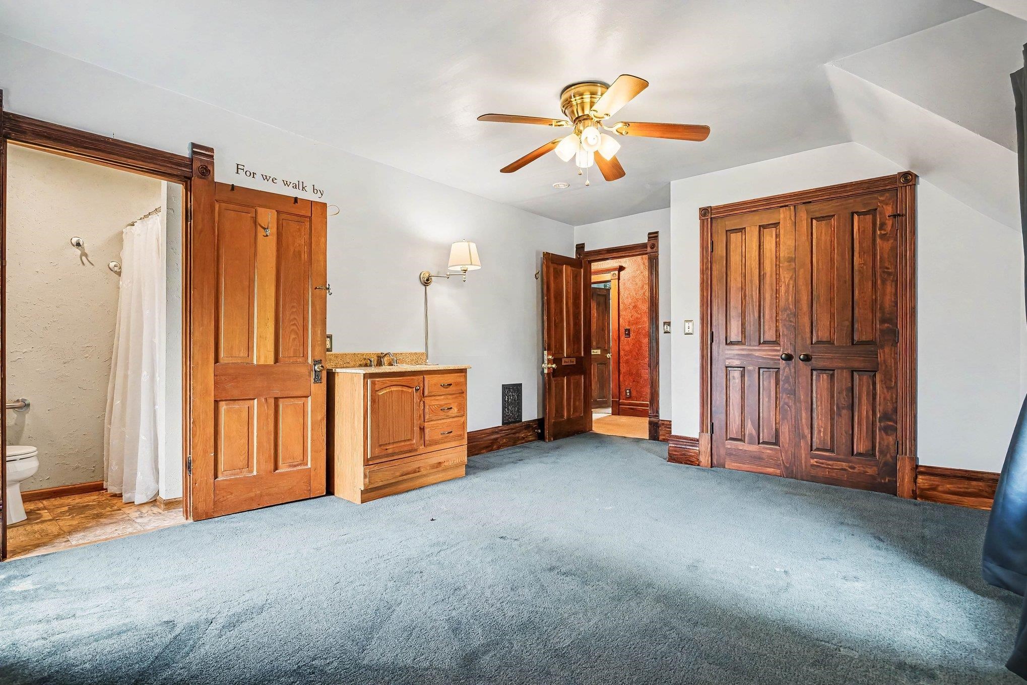 Room with blue carpeted flooring and white walls, featuring a wooden ceiling fan with integrated lighting