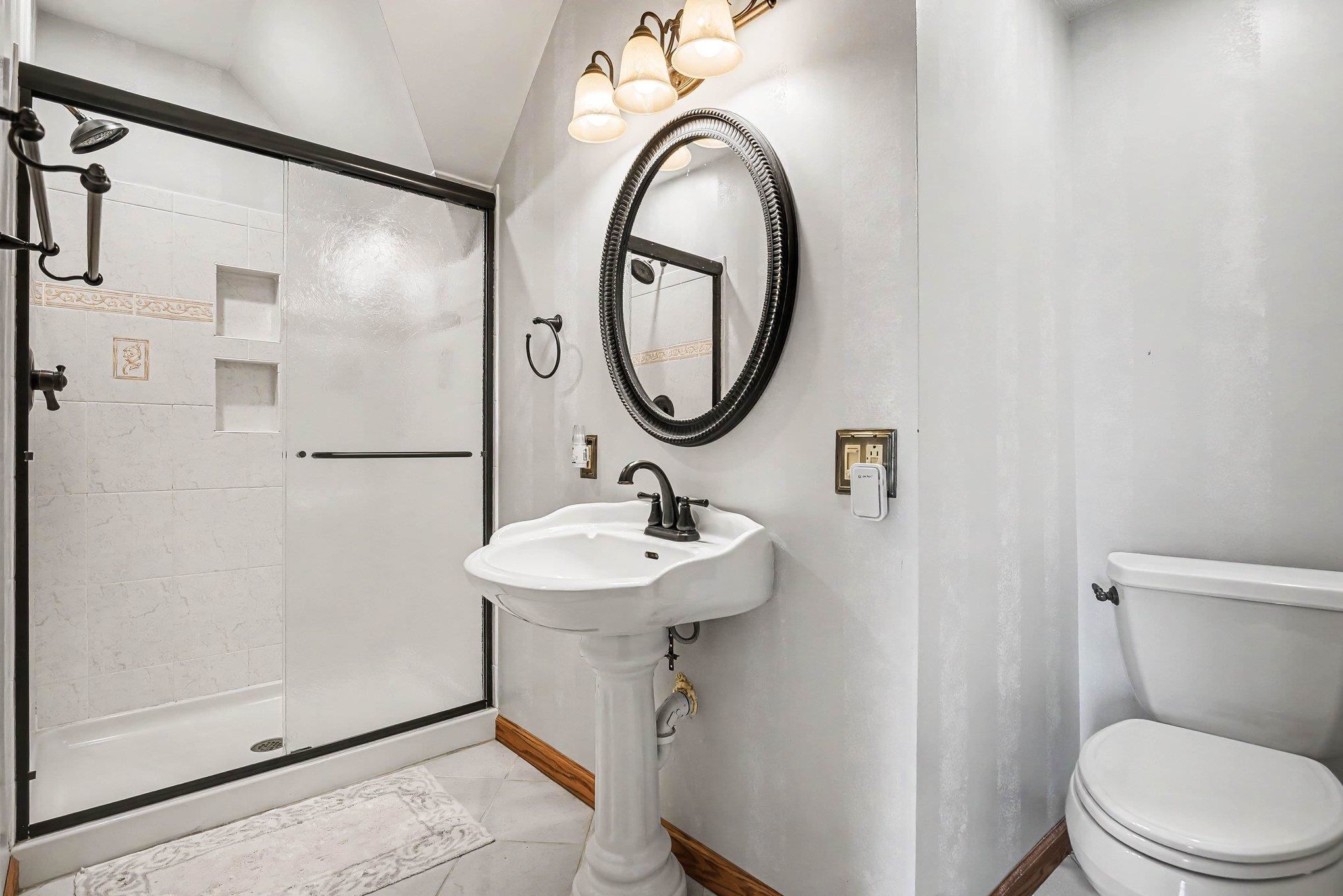 Bathroom featuring a pedestal sink, oval mirror, and a shower with sliding glass doors
