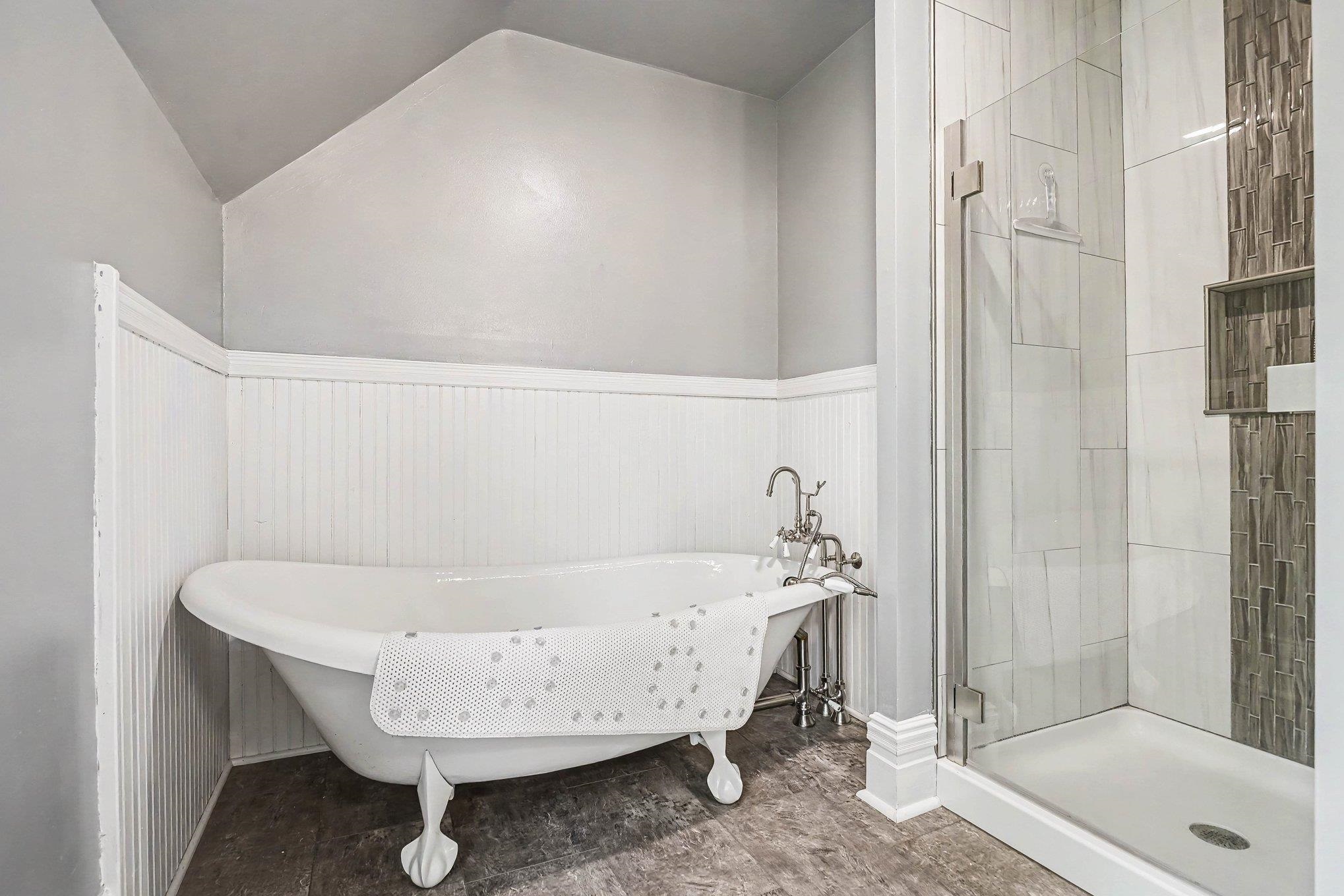 Bathroom featuring a clawfoot tub with vintage-style plumbing fixtures, a glass-enclosed shower with tiled walls and an integrated niche, beadboard wainscoting, and wood-finish flooring
