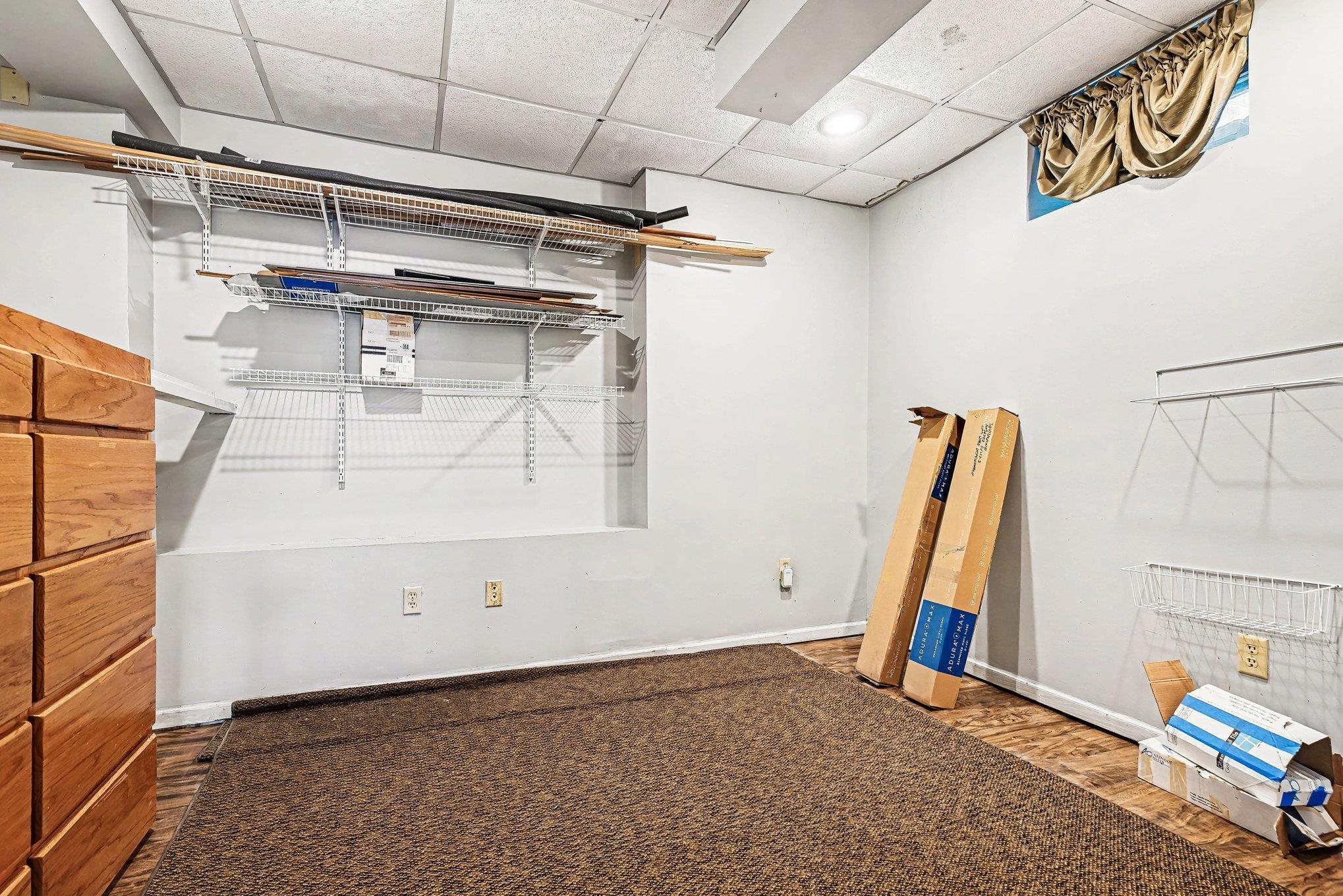 Lower level room featuring wood-finish flooring with a partial carpet overlay, white walls, and a drop ceiling with recessed lighting