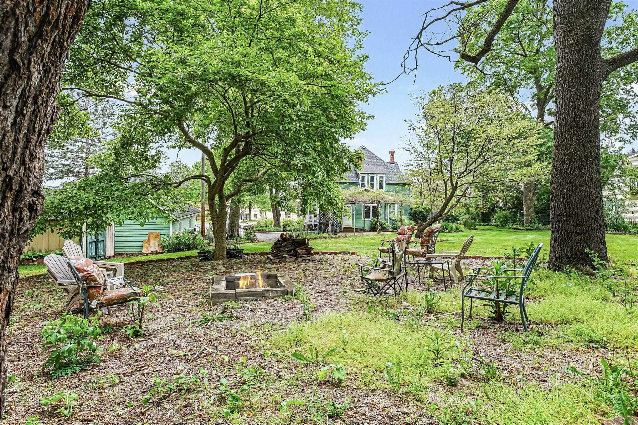 Expansive outdoor space featuring a built-in fire pit, mature trees, and a visible outbuilding
