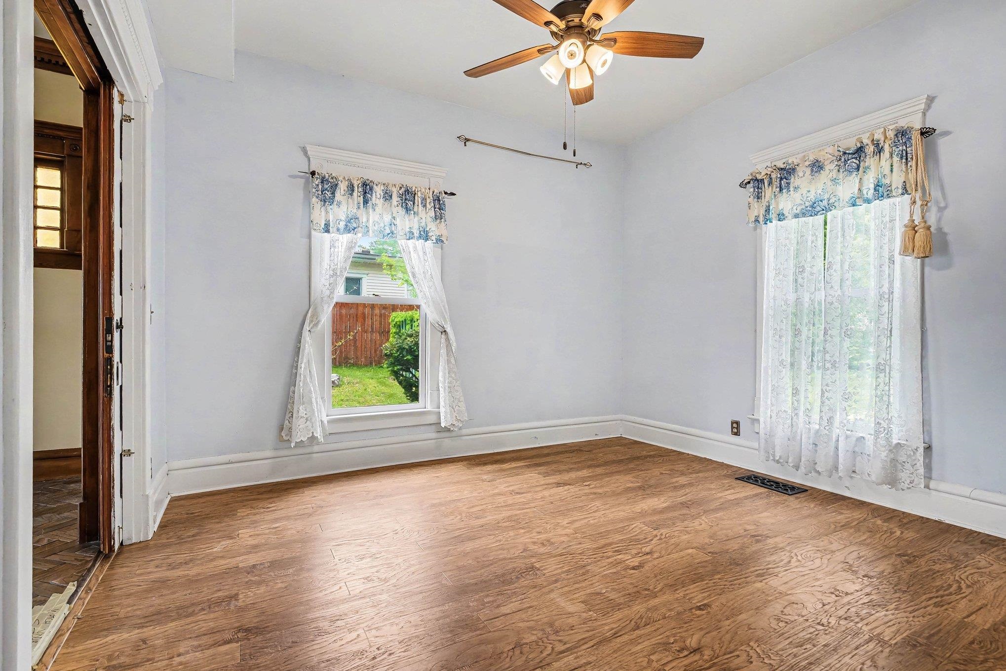 Room featuring wood-finish flooring, white baseboards, and two windows with white trim