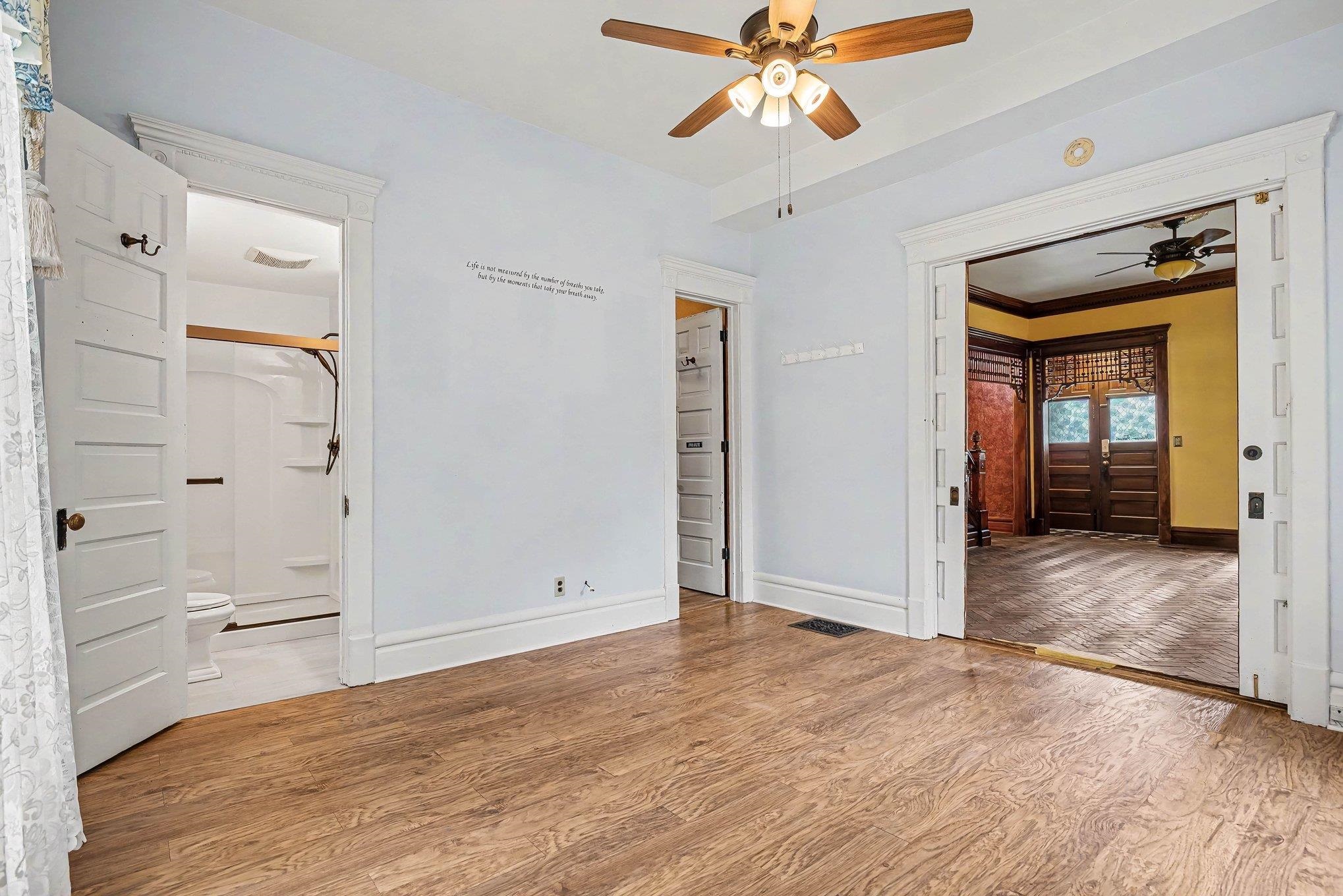 Spacious room featuring wood-finish flooring, a ceiling fan, and decorative white trim