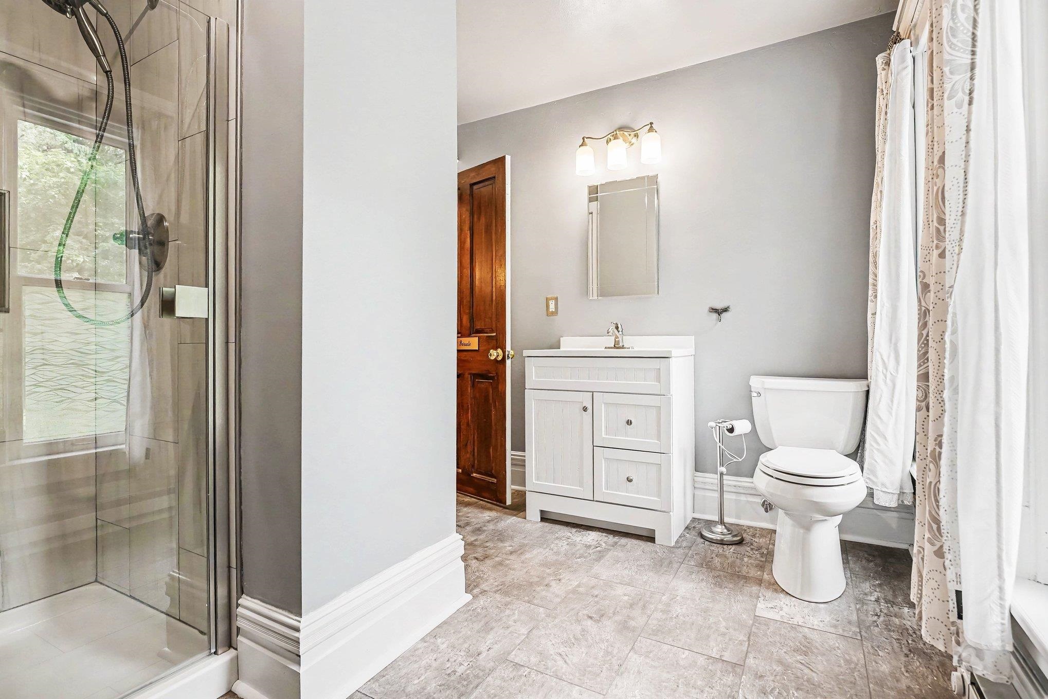 Modern bathroom featuring a glass-enclosed shower with tile surround, white vanity, and ceramic tile flooring