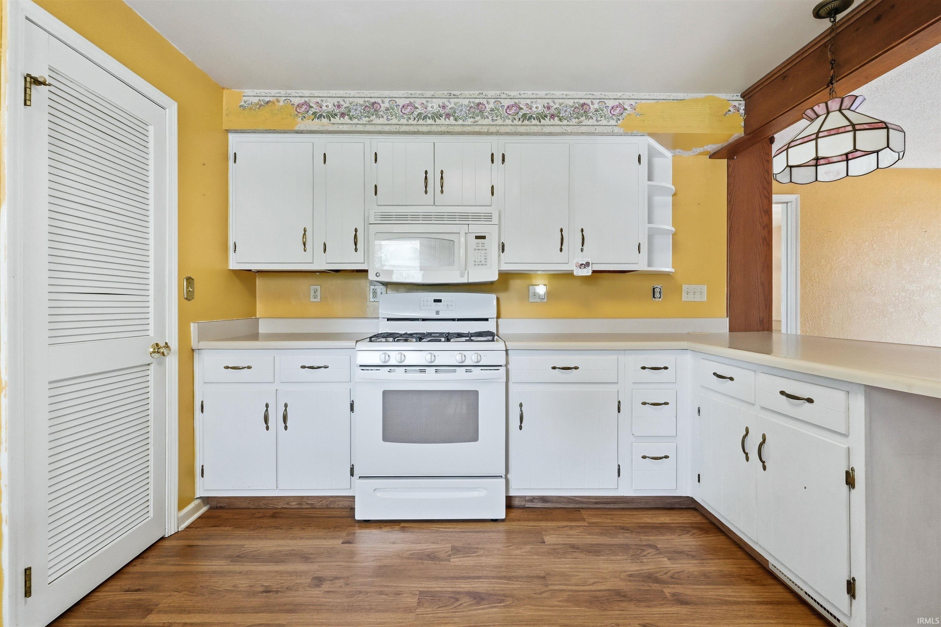 Kitchen featuring wood-finish flooring, white cabinetry with dark hardware, white gas range, and white microwave