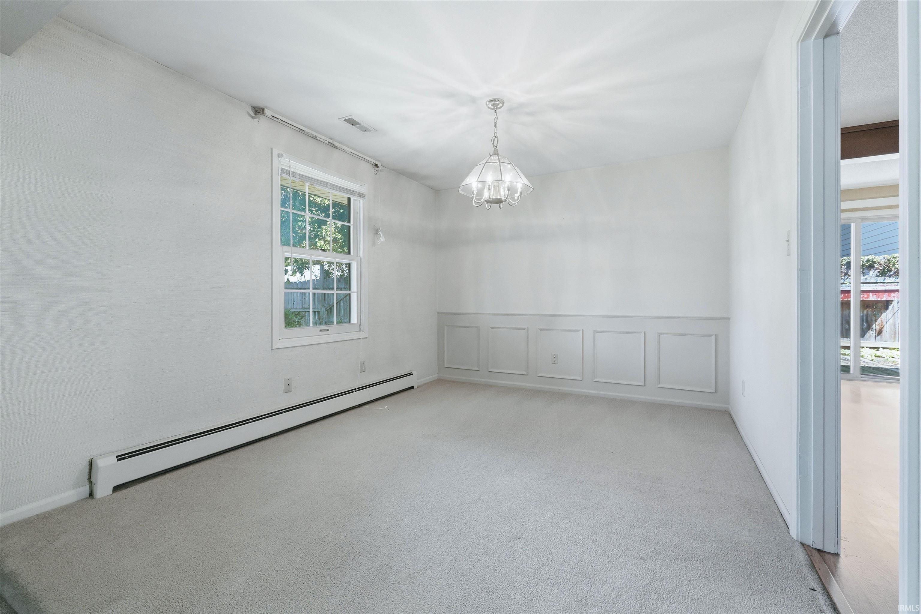 Carpeted room with a ceiling-mounted light fixture, window with exterior views, and wainscoting