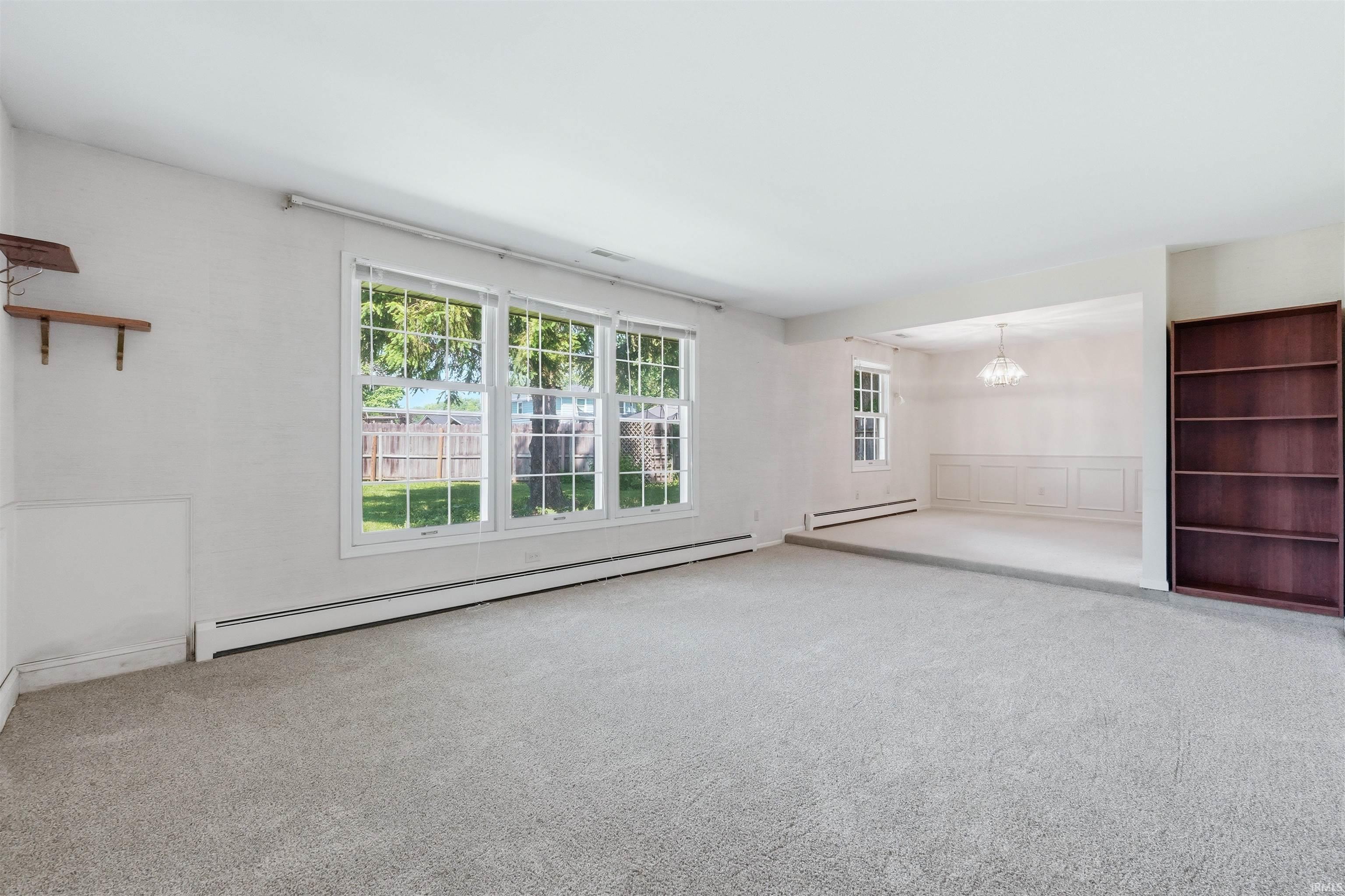 Carpeted living area featuring multiple windows, a built-in bookshelf, and a step-down entryway to an additional room with wainscoting and an overhead light fixture