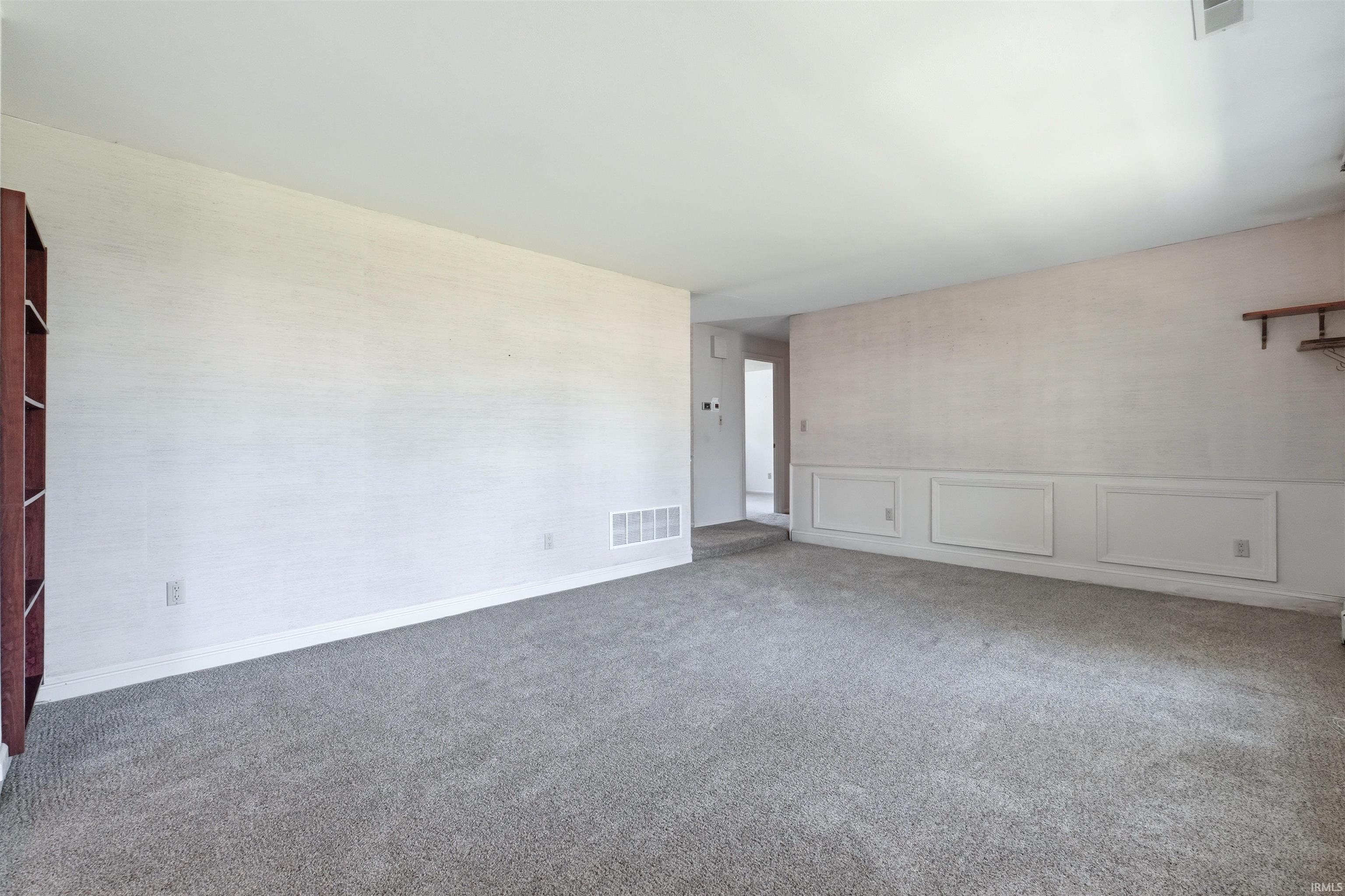 Spacious room with plush gray carpeting, white baseboards, and wainscoting details