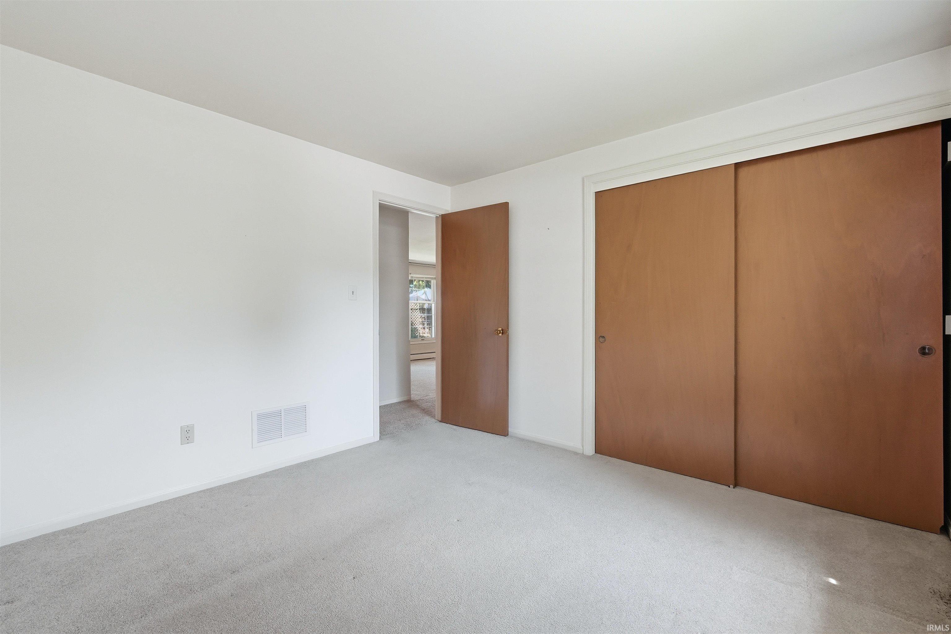 Room featuring light-toned carpeting, white walls, and a wood-finish sliding door closet