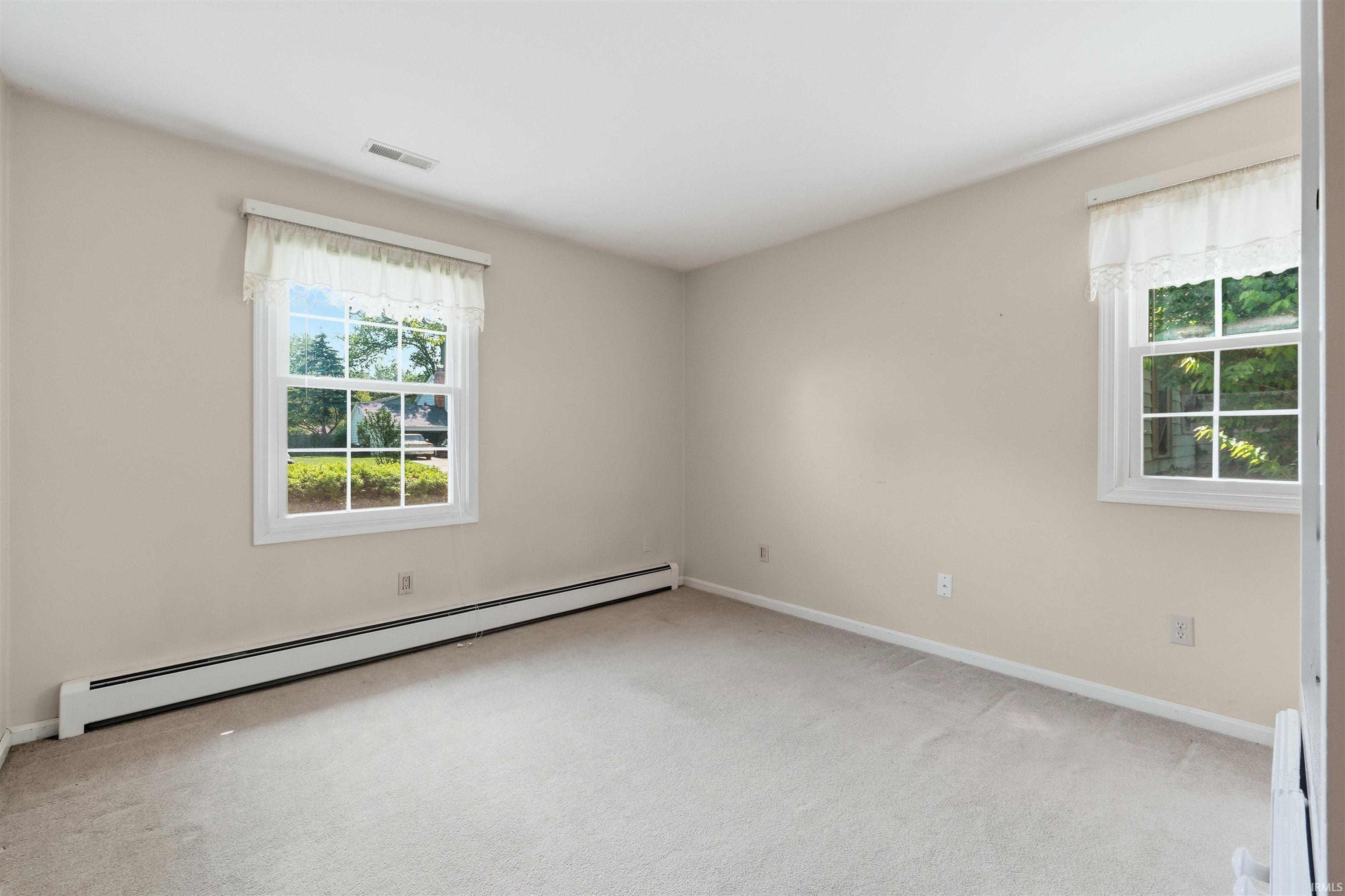 Interior room with light tan walls, two white-framed windows, and light-colored carpeting