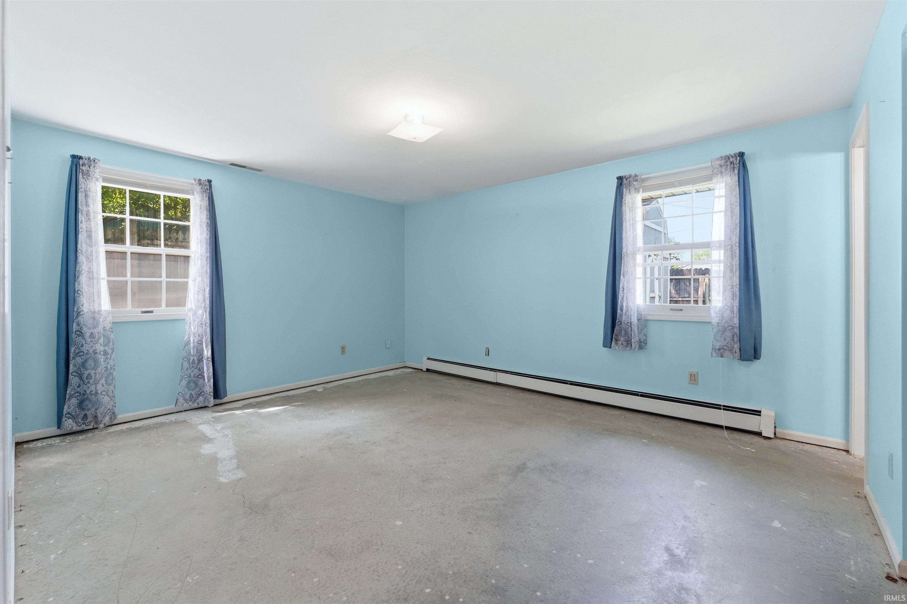 Spacious room featuring light blue walls and two windows with white grilles