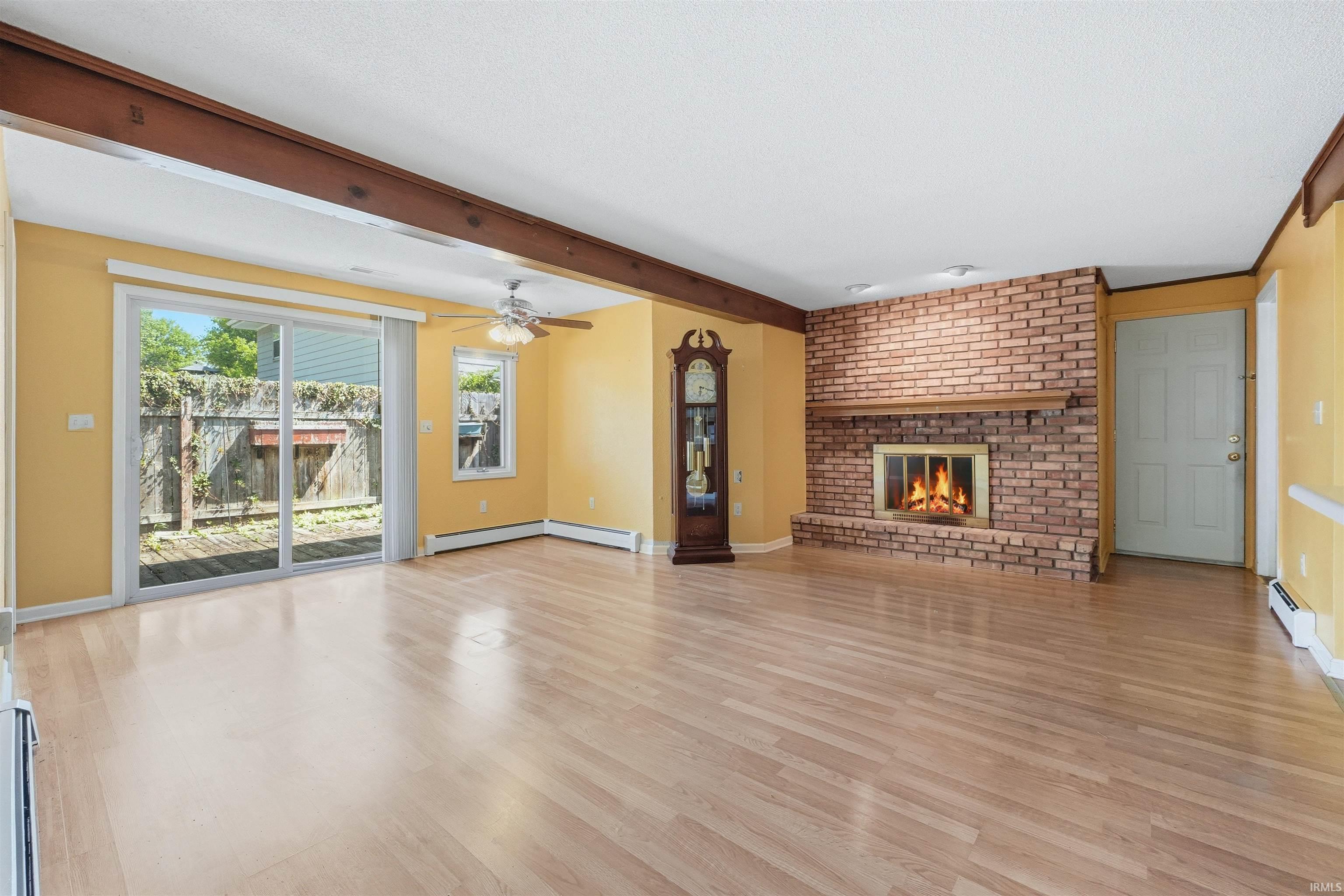 Spacious living area featuring wood-finish flooring, a brick fireplace with a wood mantle, and exposed ceiling beams