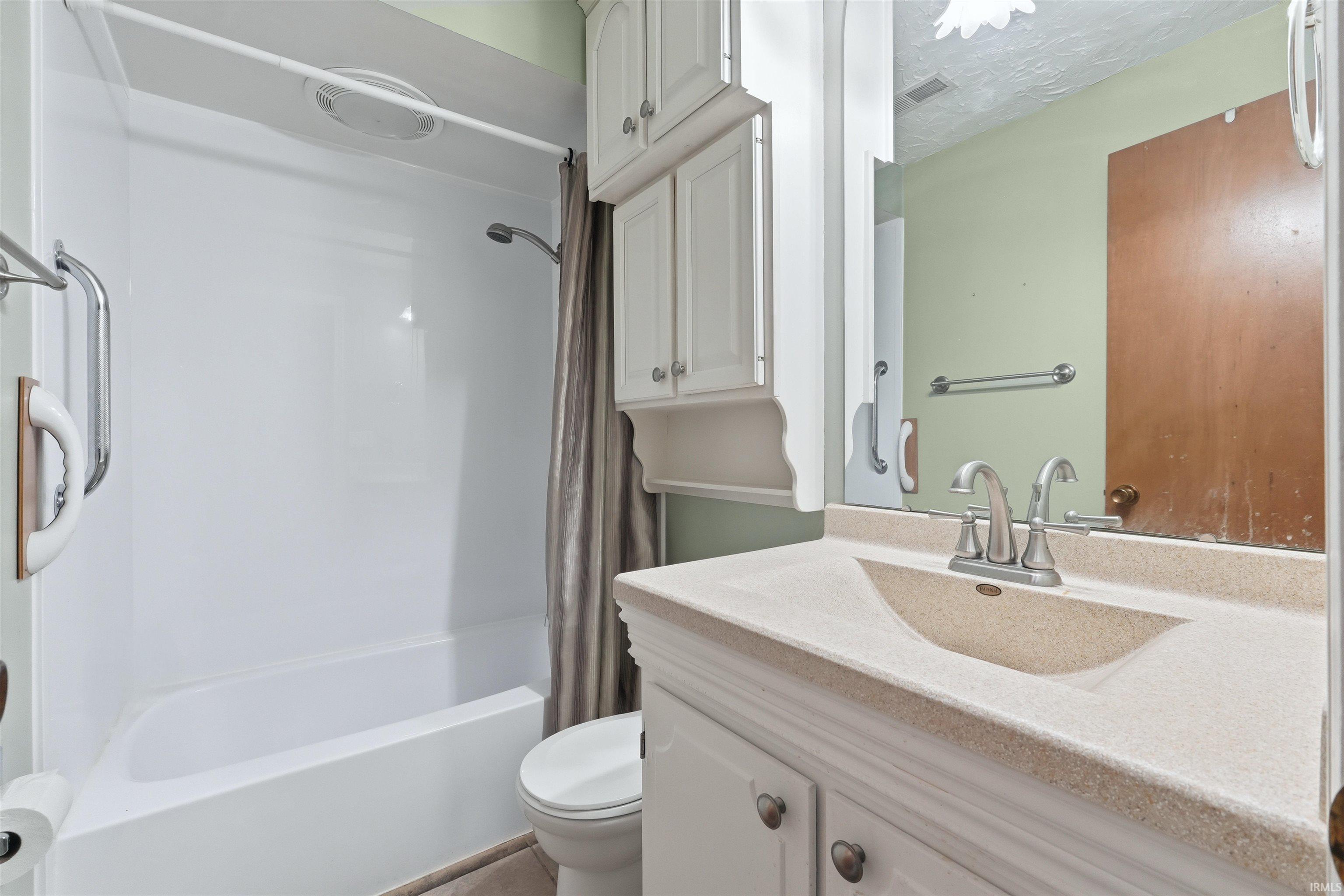 Bathroom featuring a white tub/shower combination with grab bars, a vanity with an integrated sink and light-colored countertop, and white cabinetry