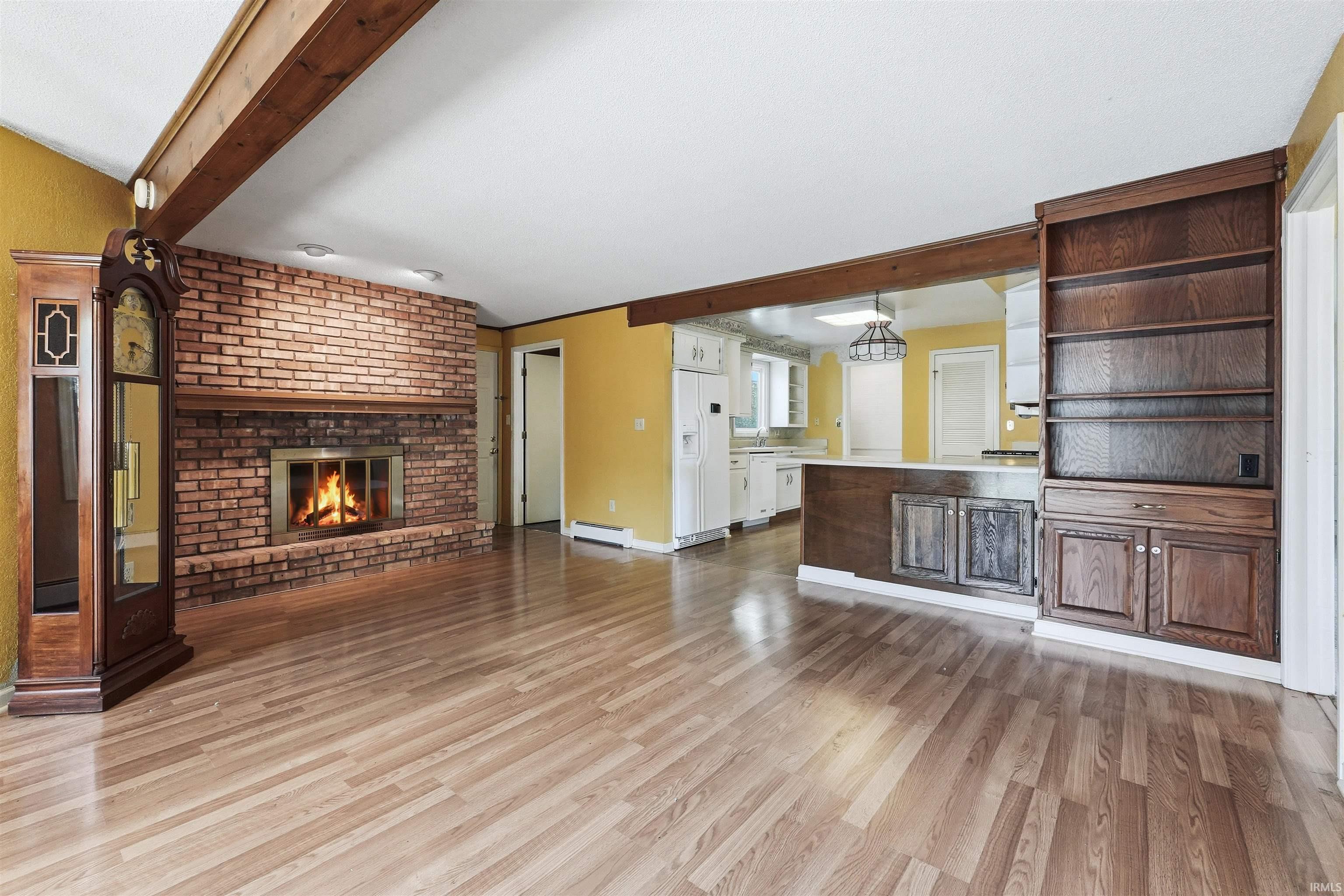 Spacious living area featuring wood-finish flooring, a brick fireplace with a raised hearth, and exposed wood beams