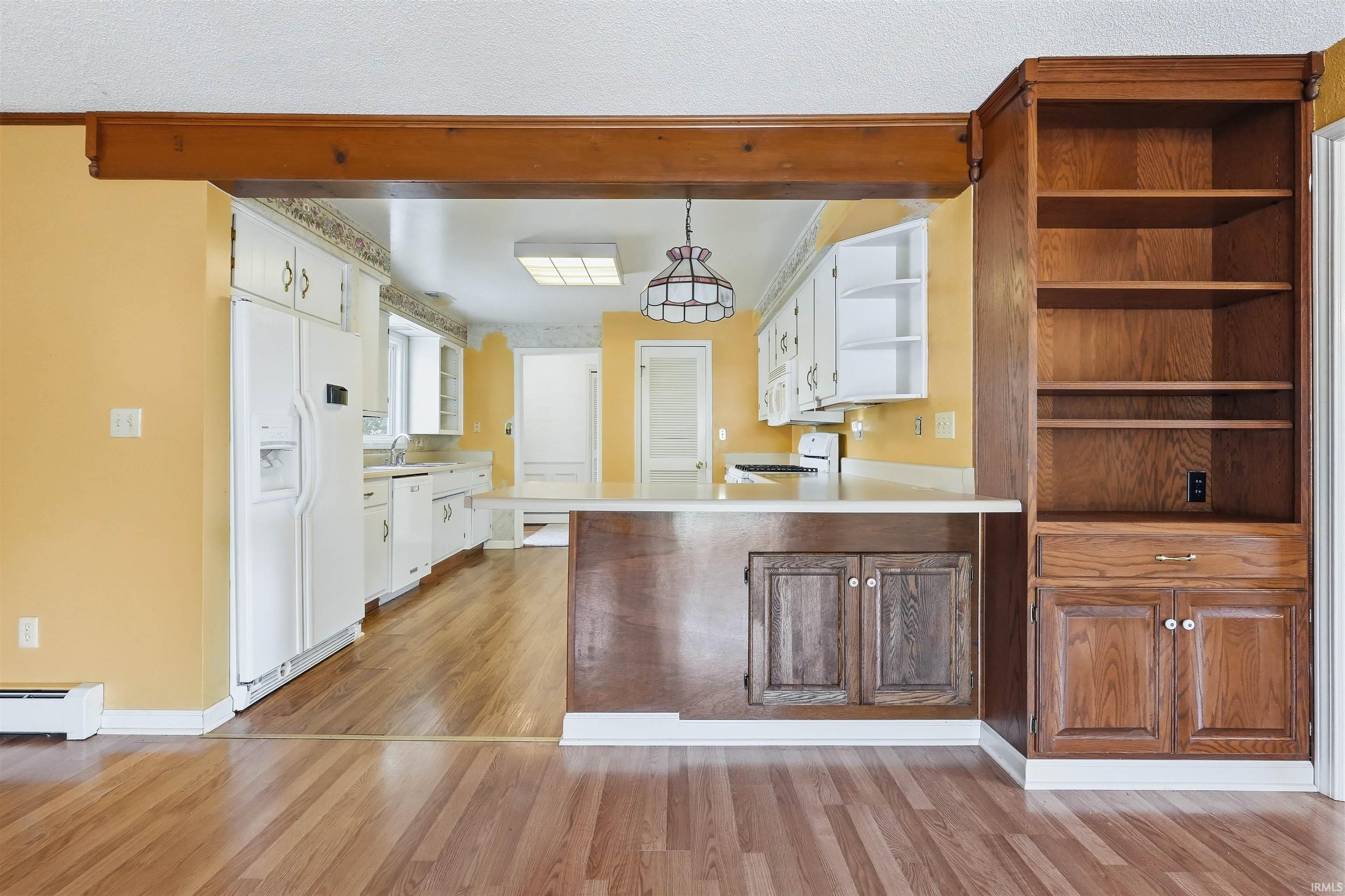 Kitchen area with wood-finish flooring, white cabinetry, and a peninsula counter