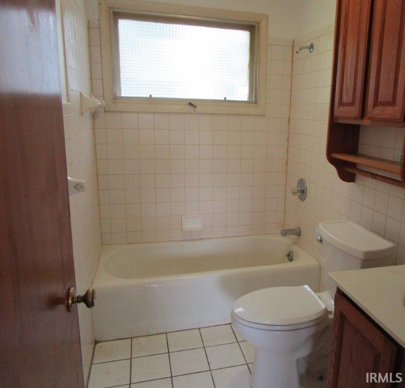 Full bathroom featuring a window, a white bathtub, ceramic wall tiling, a toilet, and a wood-finish vanity with a countertop