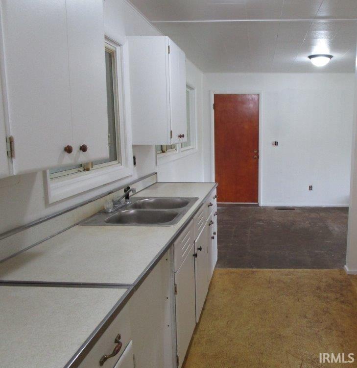 Kitchen area featuring white cabinetry, a dual basin sink with a single-handle faucet, and light-toned countertops with metal trim