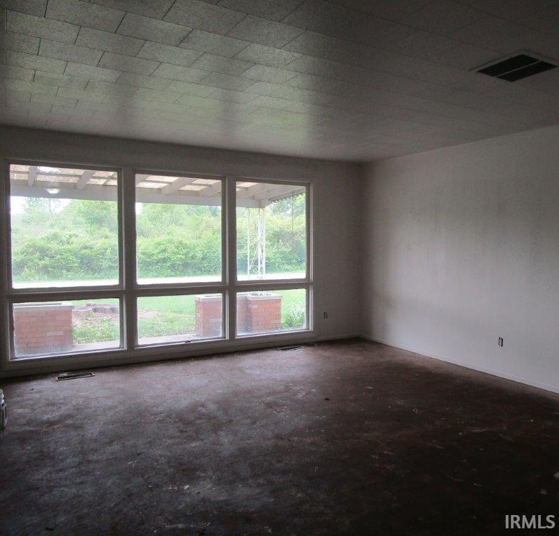 Spacious interior room with multiple large windows overlooking exterior greenery and a covered porch
