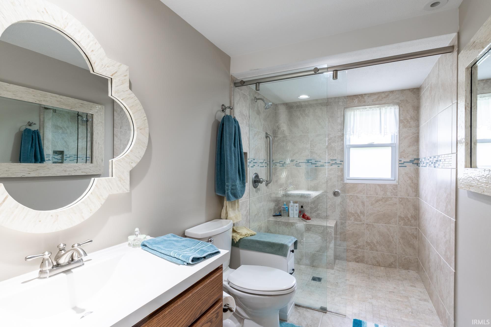 Spacious bathroom featuring a glass-enclosed shower with tiled walls, built-in shelving, and a window
