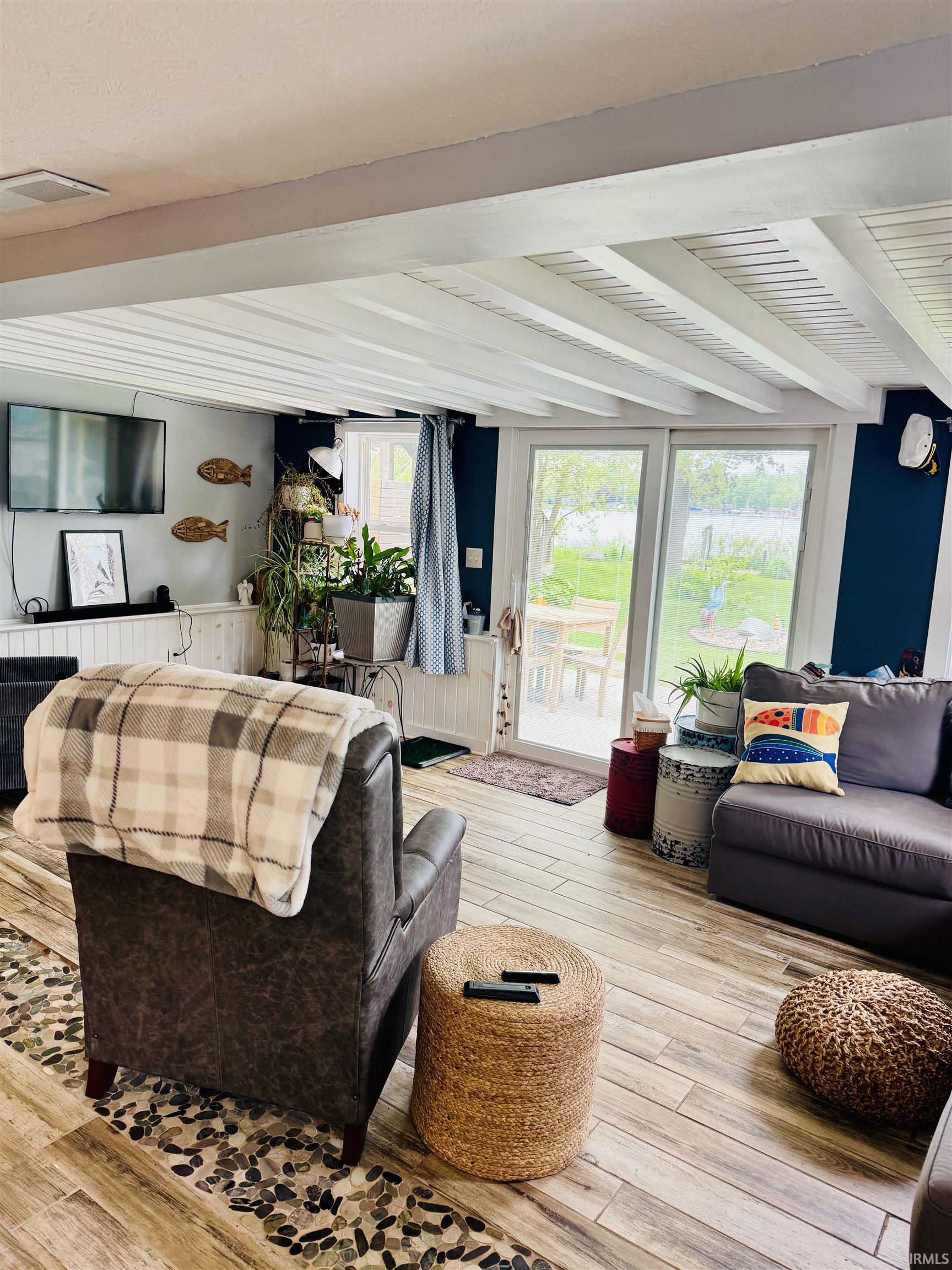Wood-finish flooring with a decorative pebble inlay, exposed ceiling beams, and a wall of glass doors opening to the exterior