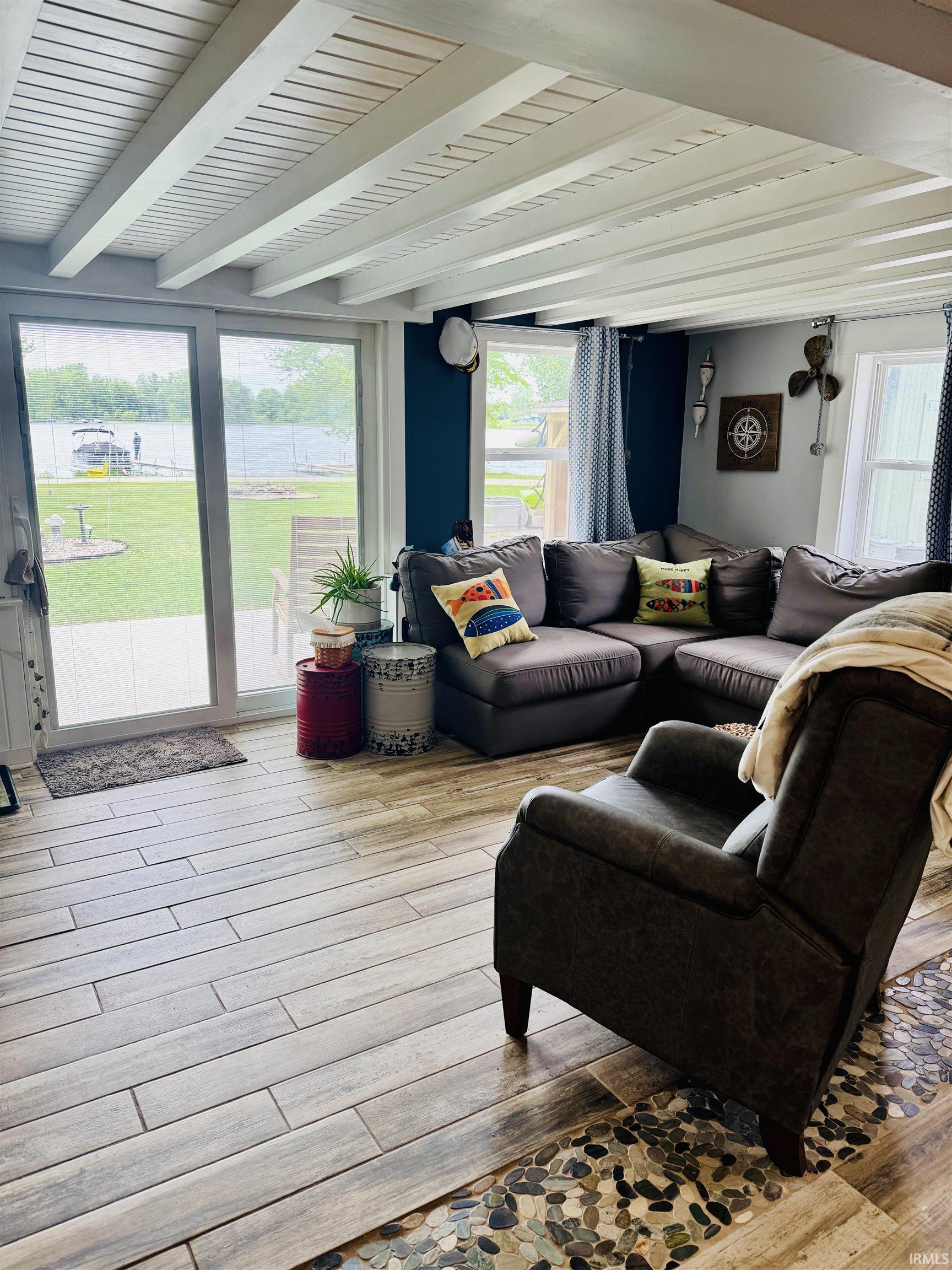 Living area featuring a water view, white exposed beam ceiling, wood-finish flooring, full-light patio doors, and a stone pebble floor inlay