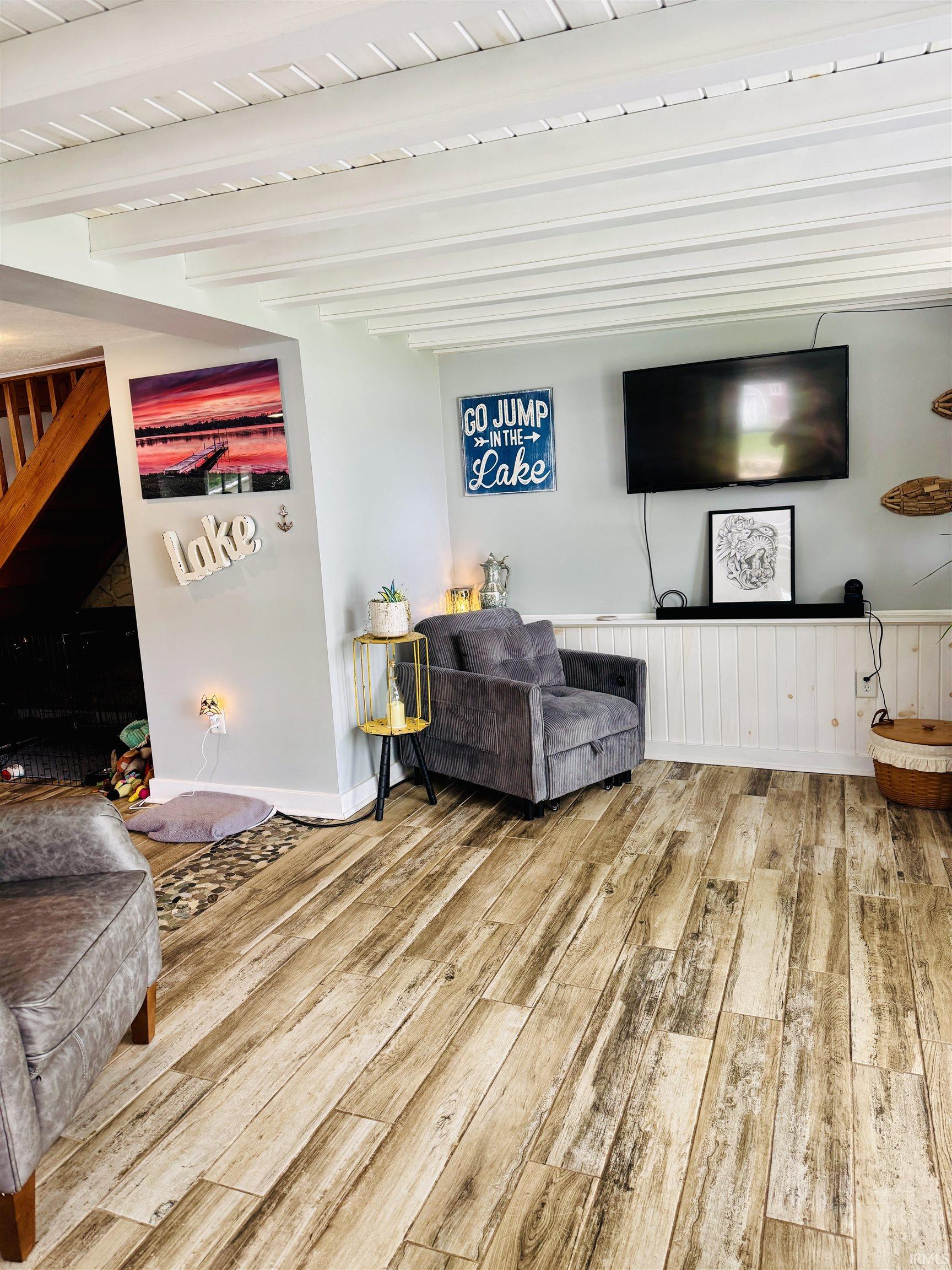 Interior space featuring wood-finish flooring, white exposed beam ceiling, light blue walls, and white wainscoting