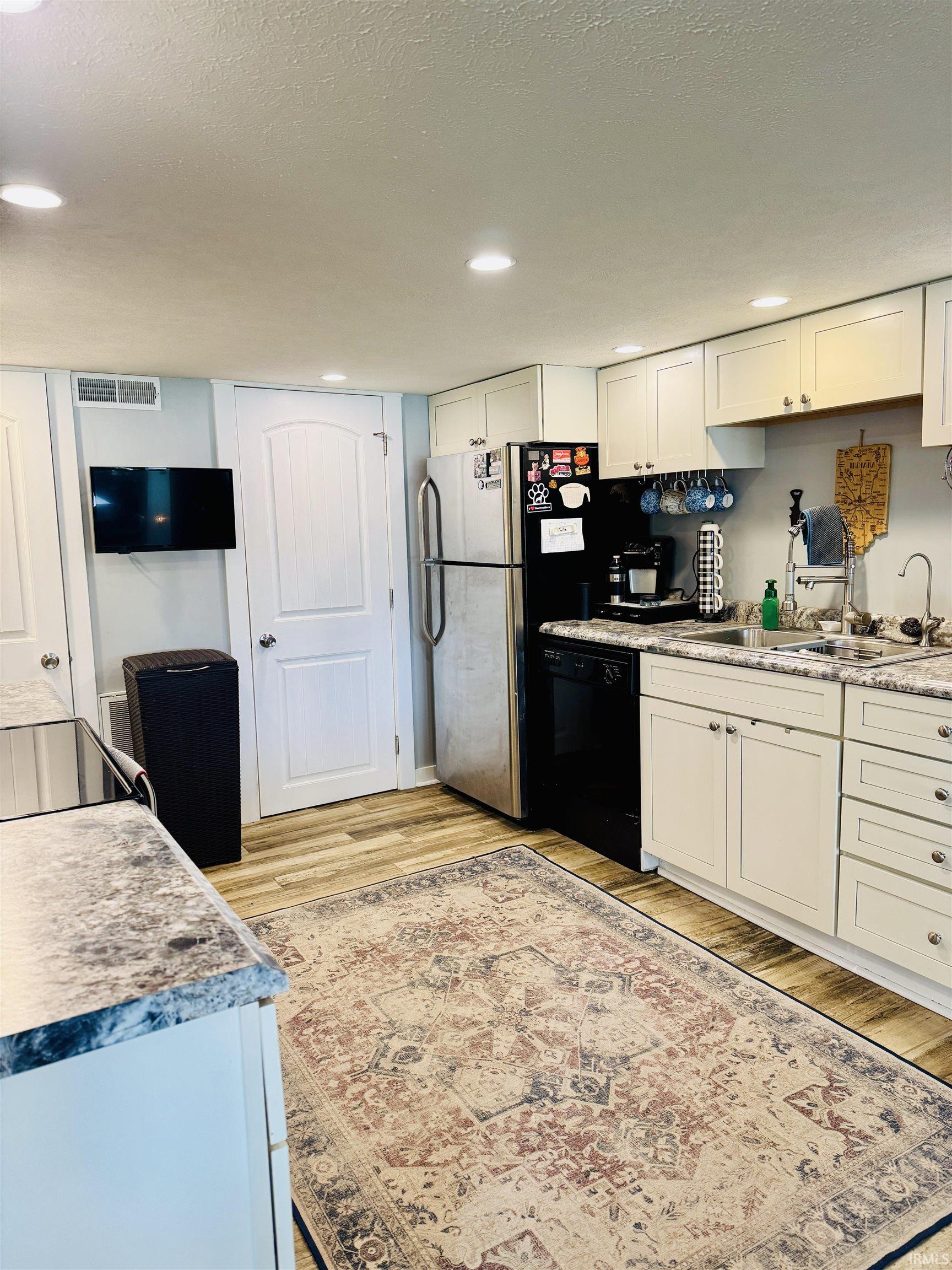 Kitchen featuring light-toned cabinetry, wood-finish flooring, recessed lighting, stainless steel refrigerator, and integrated sink