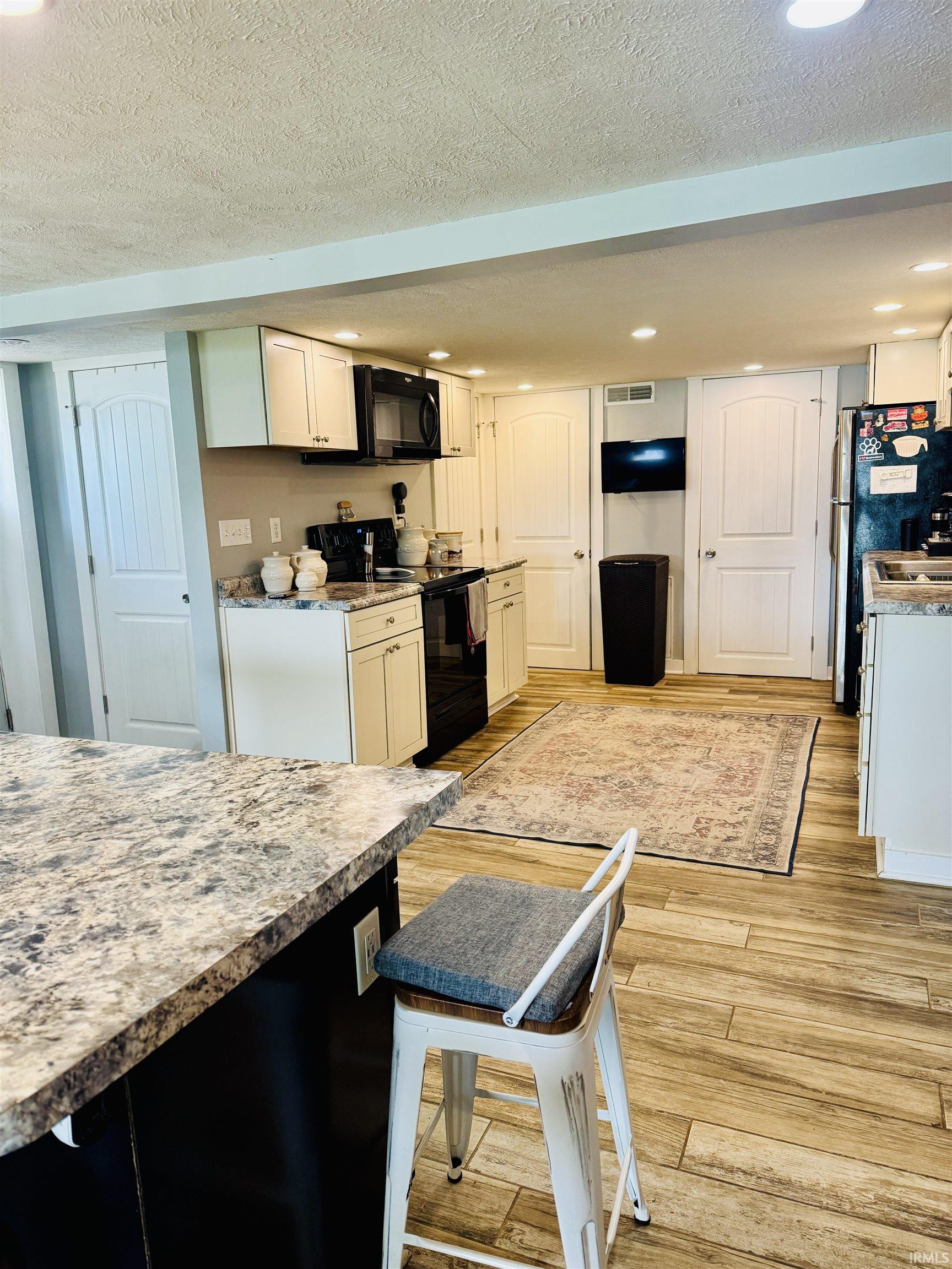 Kitchen featuring a peninsula with a patterned countertop, wood-finish flooring, recessed lighting, and white cabinetry with black hardware