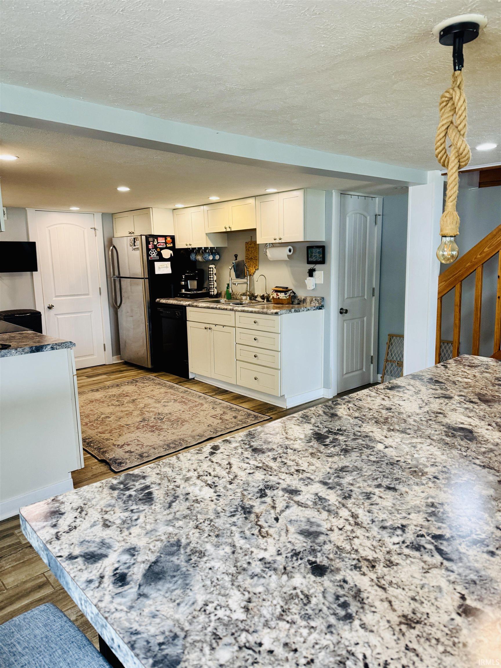 Kitchen featuring white cabinetry, a double-basin stainless steel sink, wood-finish flooring, and light-toned countertops