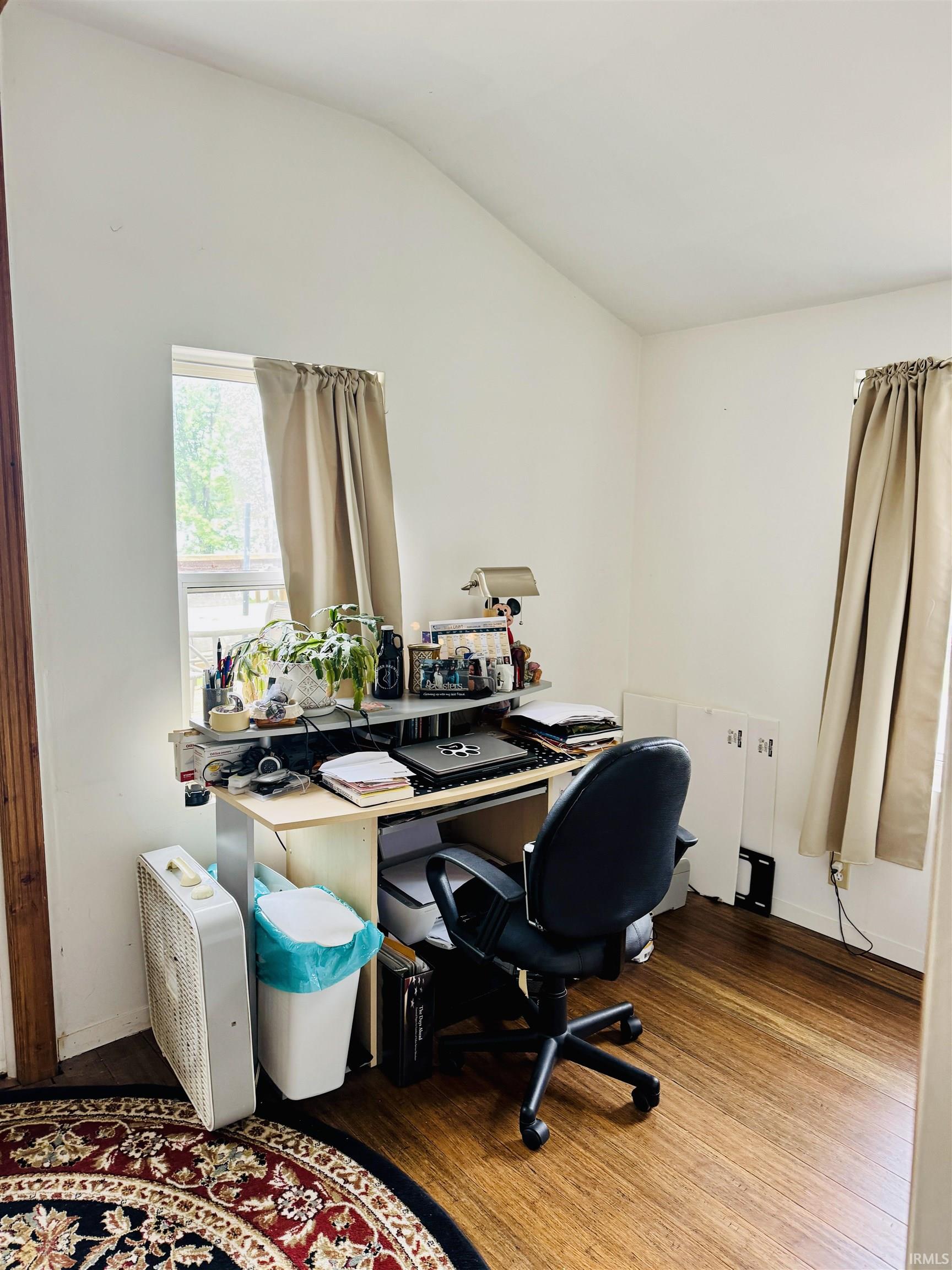 Vaulted ceiling room featuring wood-finish flooring and multiple windows