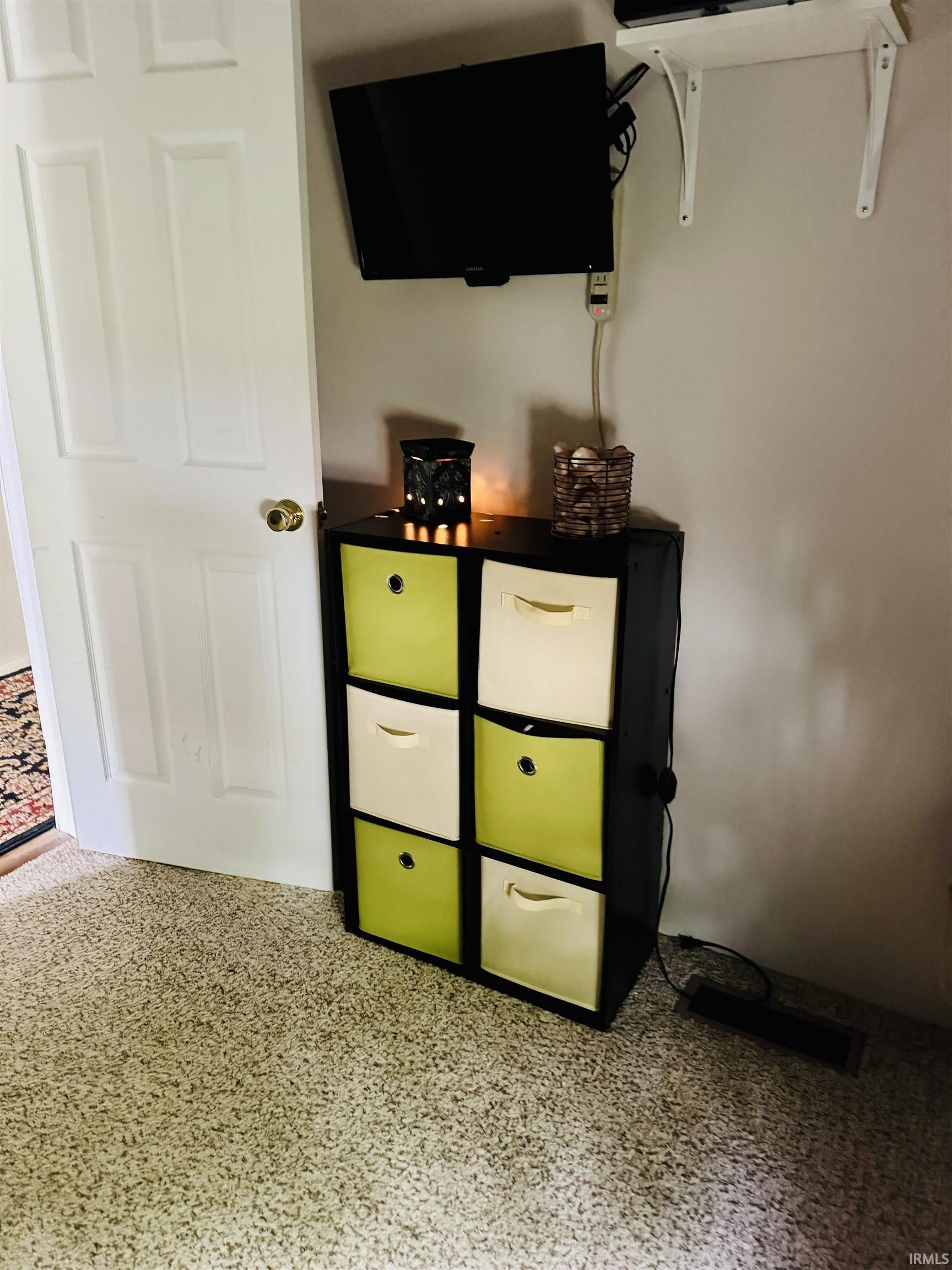 Wall-mounted television with white shelving, light-colored wall, and textured carpeting