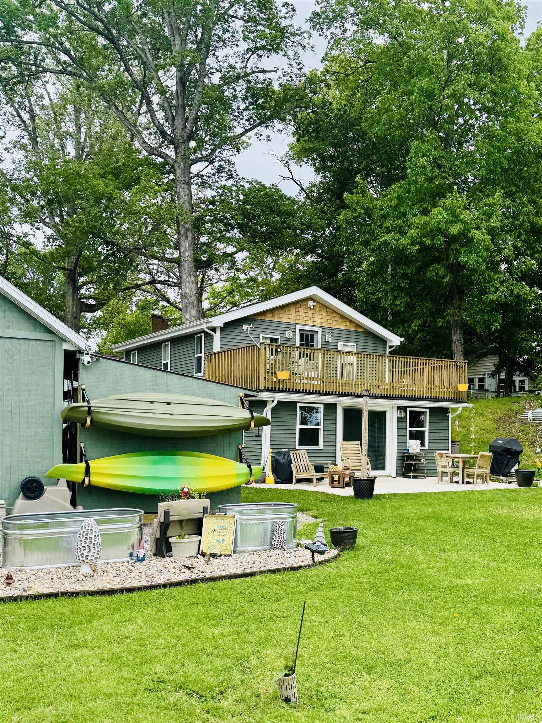 Two-story dwelling with dark green siding, an upper-level deck with wood railing, and a lower-level patio