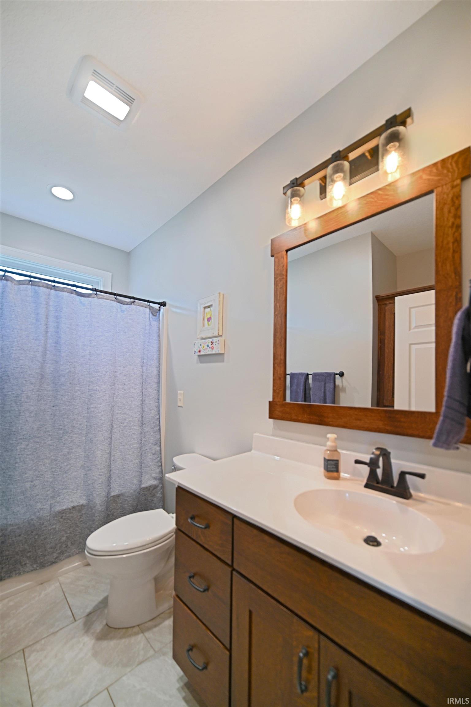 Bathroom featuring a wood-finish vanity with a white countertop and integrated sink, matte black faucet, and a rectangular framed mirror with a three-light fixture