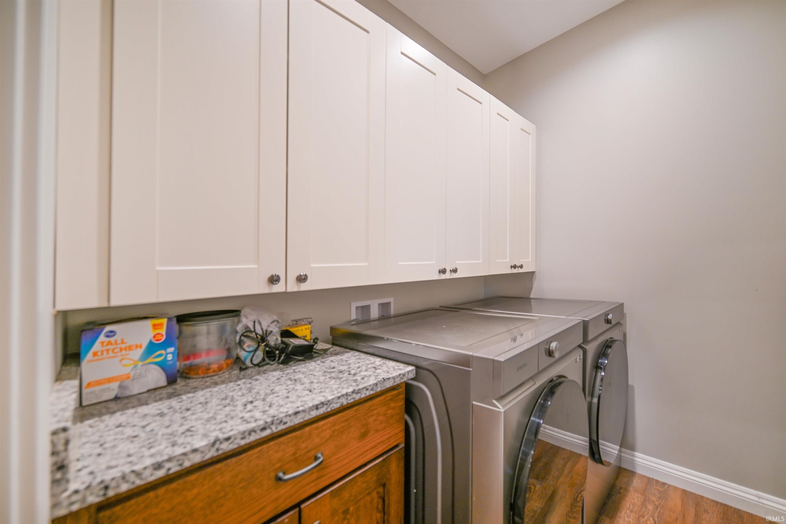 Dedicated laundry area featuring white shaker-style cabinetry, granite-finish countertops, wood-finish flooring, and light neutral wall paint