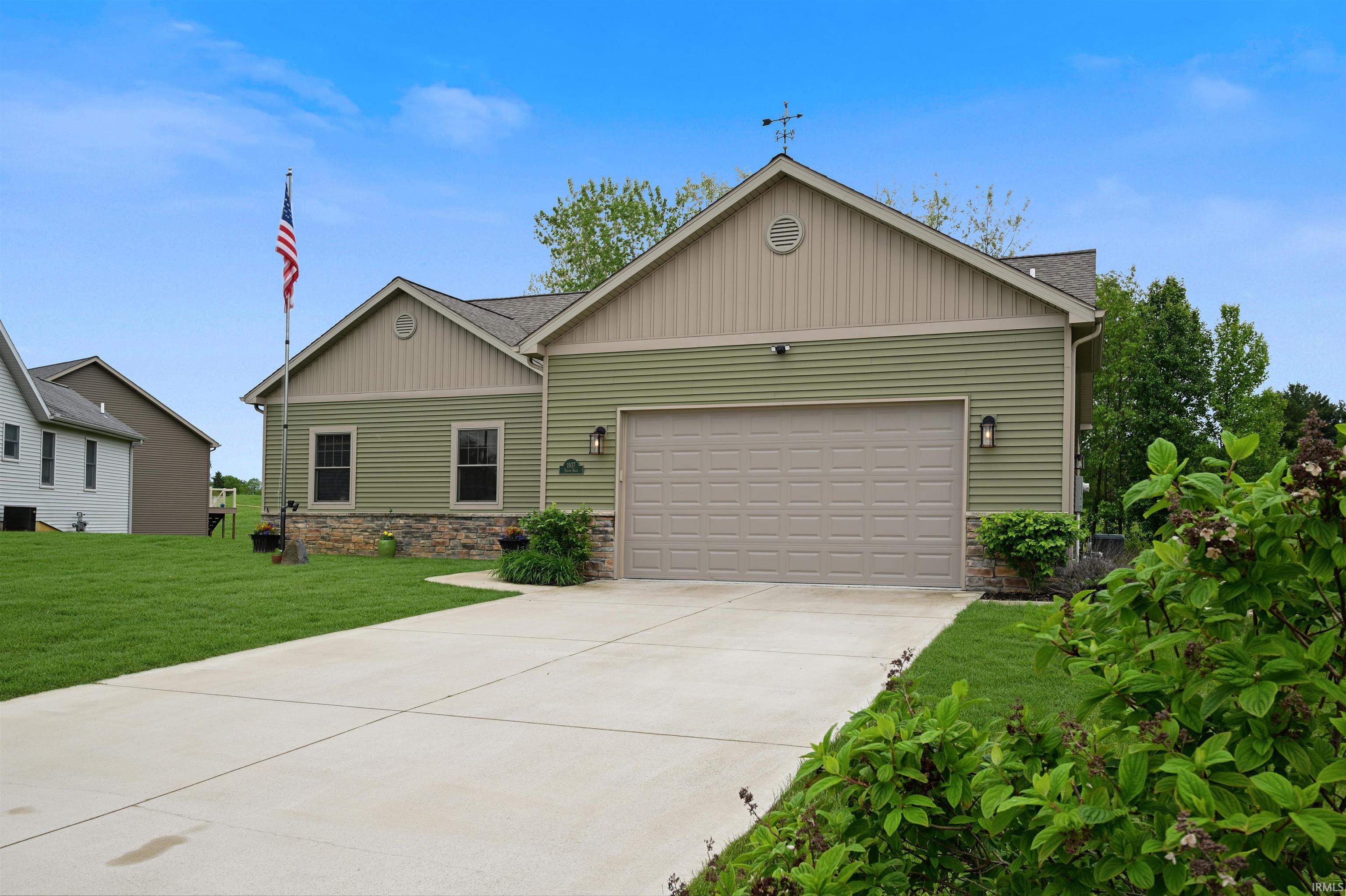 Exterior featuring green horizontal siding, stone veneer accents, and a light-colored garage door