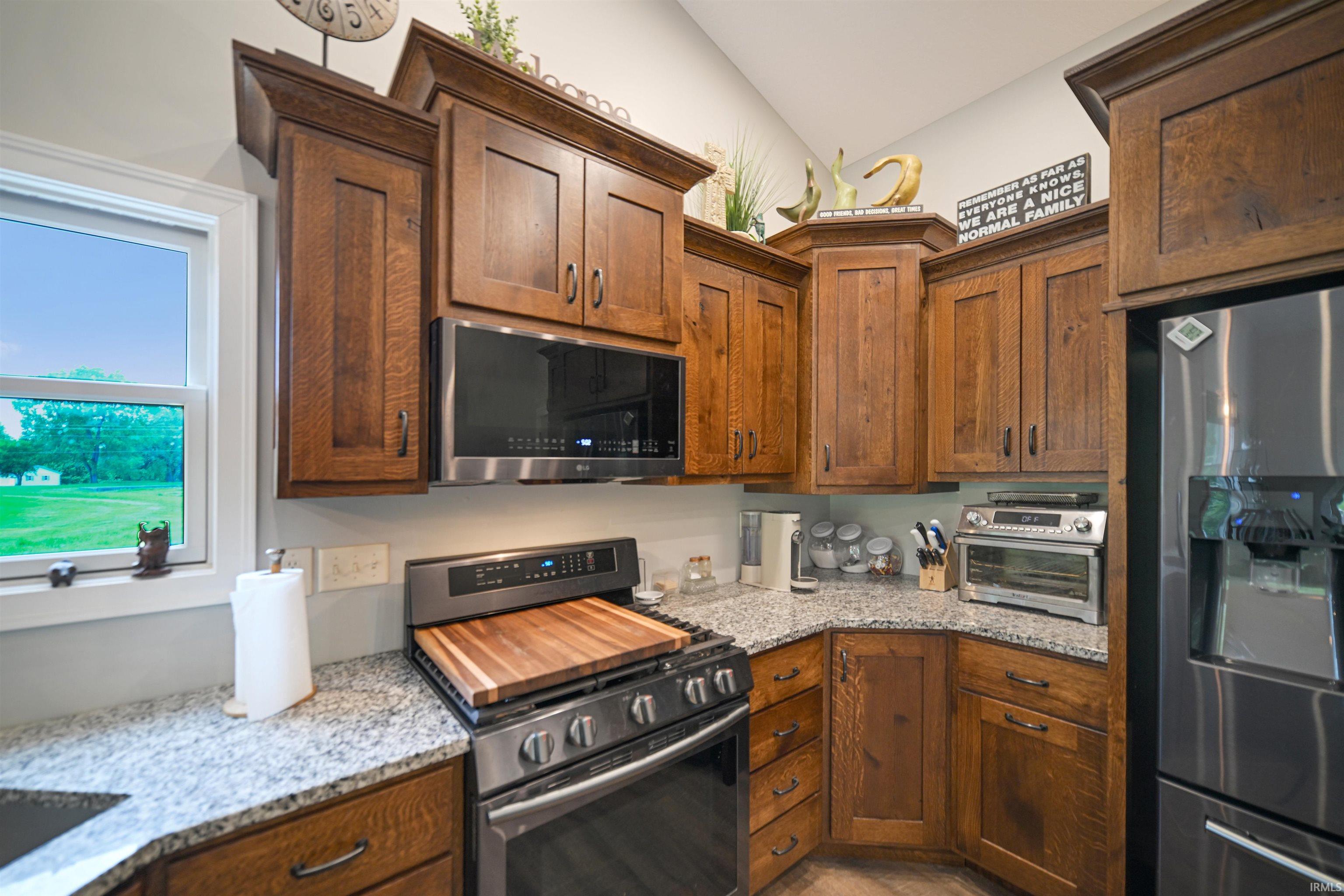 Kitchen featuring granite countertops, wood-finish cabinetry, stainless steel appliances, and an undermount microwave