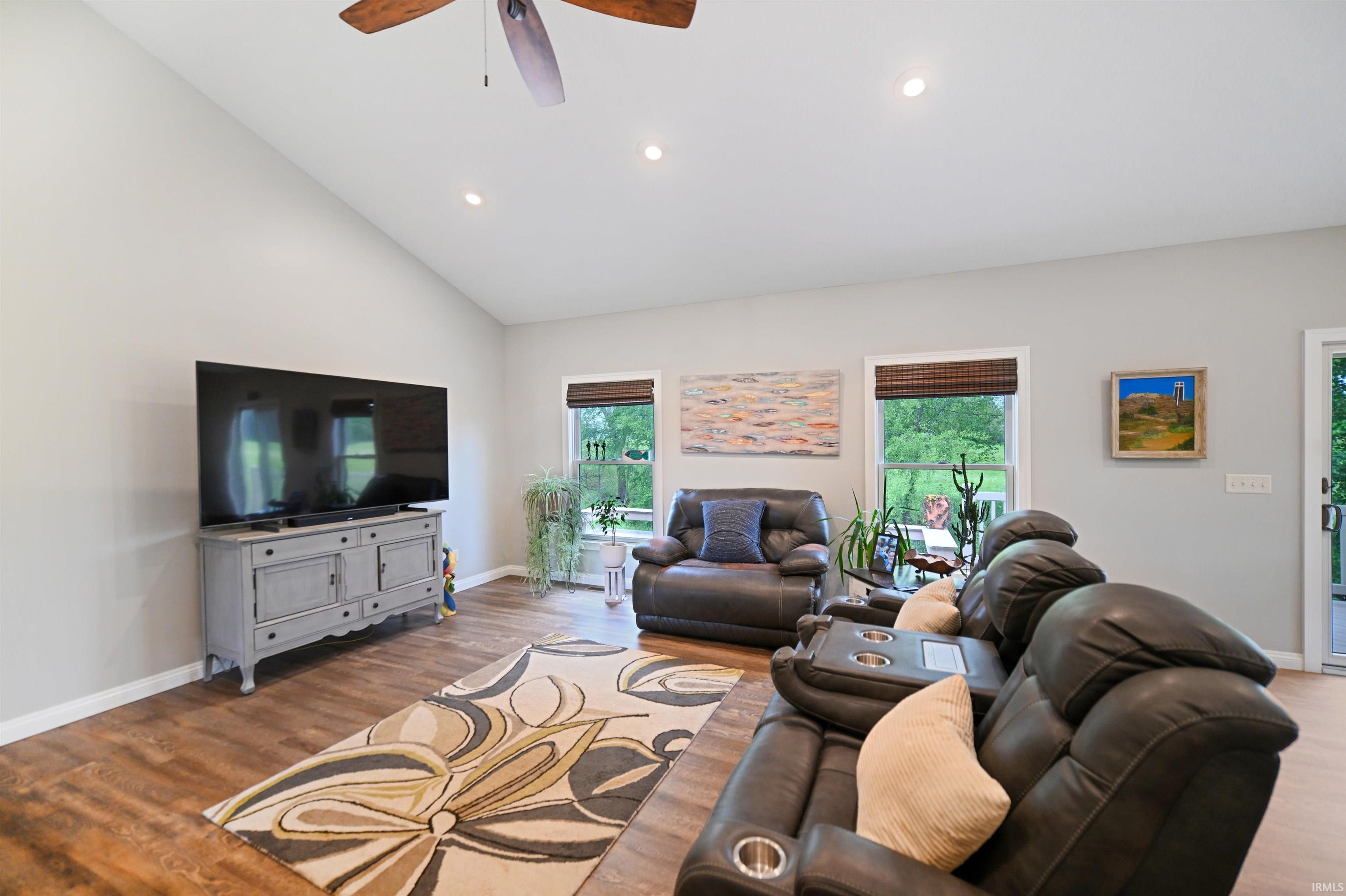 Spacious living area featuring a vaulted ceiling with a ceiling fan, recessed lighting, wood-finish flooring, and multiple windows with woven shades