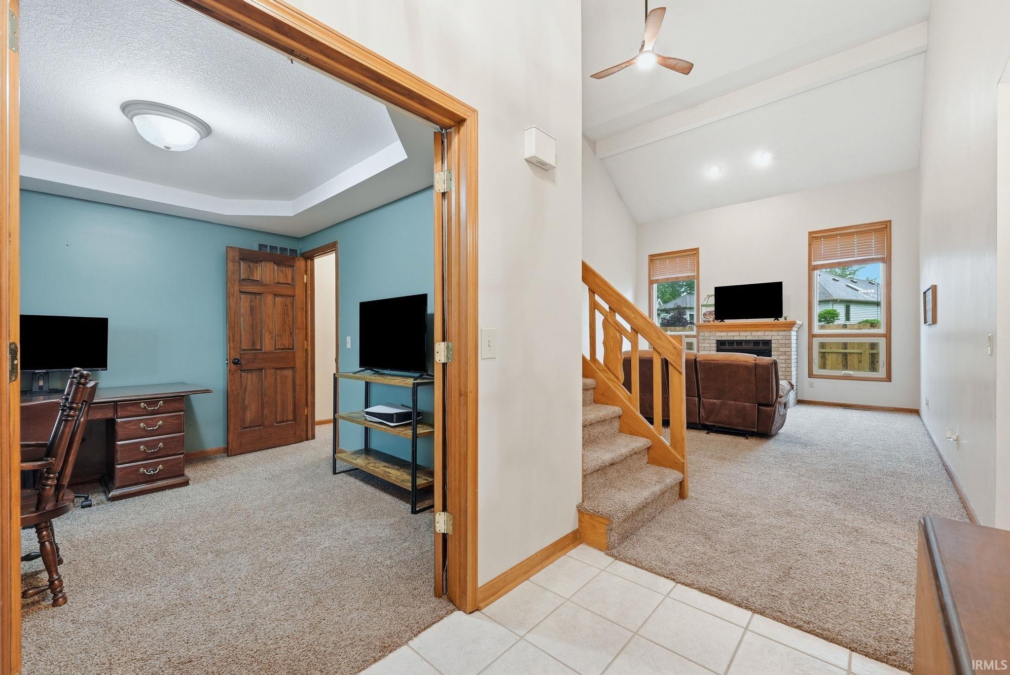 Spacious living area featuring a vaulted ceiling with exposed beams, ceiling fan, and carpeted flooring