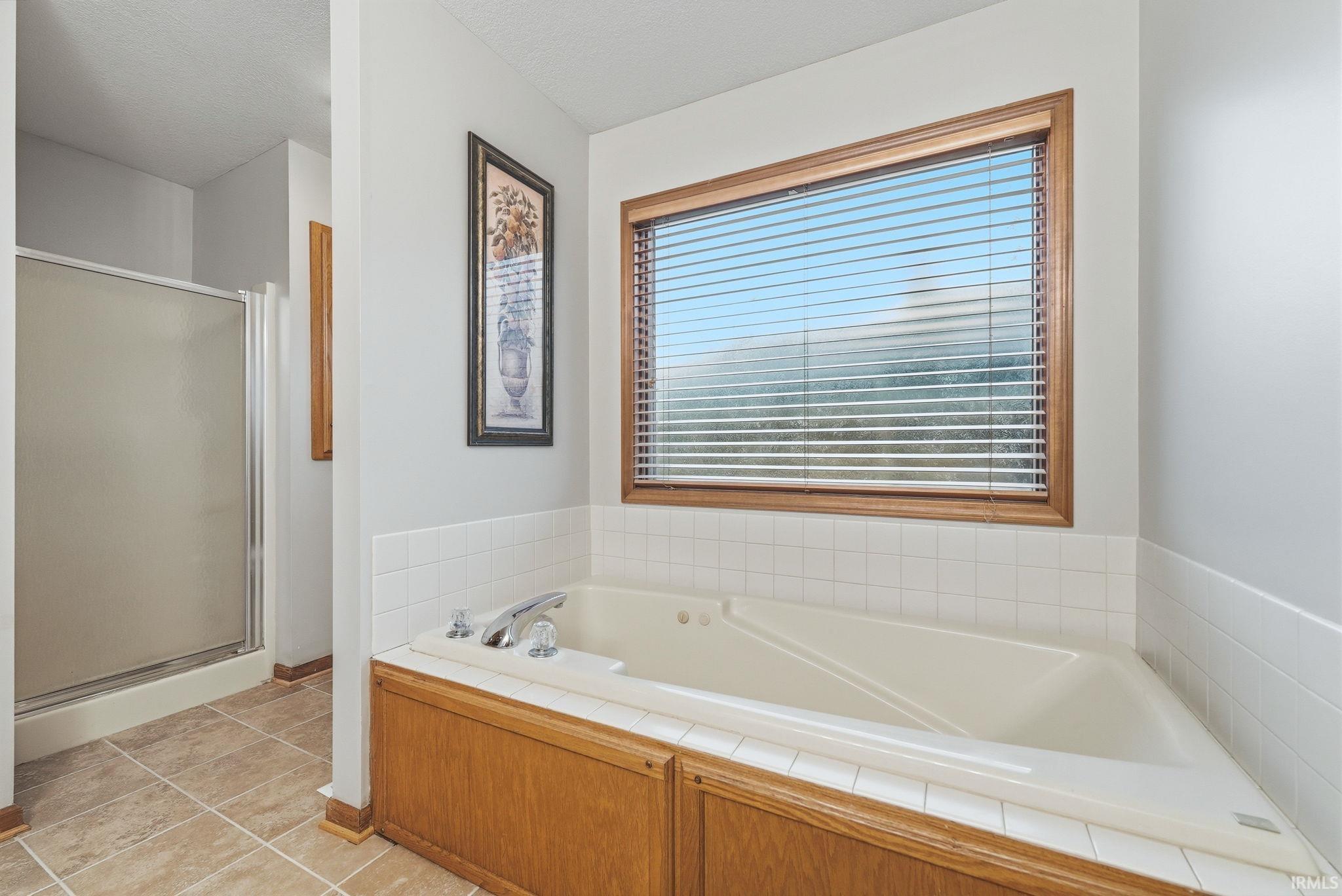 Corner soaking tub with a tiled surround, wood-finish paneling, and polished chrome fixtures