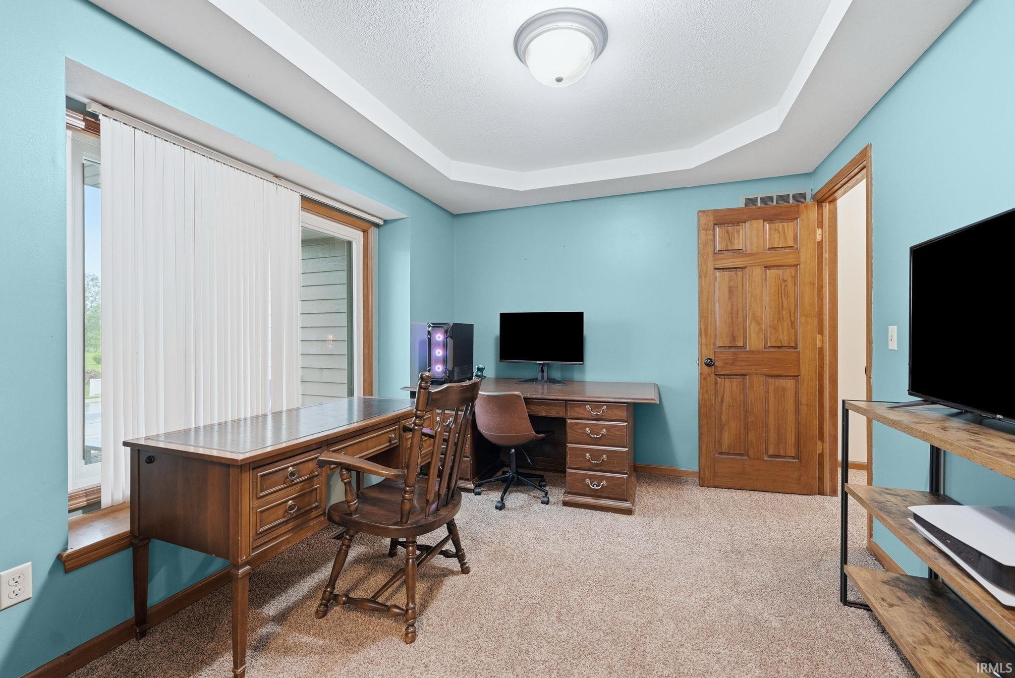 Room featuring a tray ceiling, light blue walls, and textured carpet flooring
